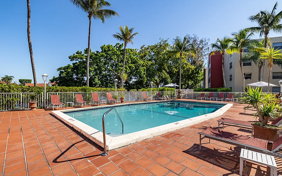 Inviting outdoor pool area with sun loungers, surrounded by lush greenery and tall palm trees, perfect for relaxation and leisure.