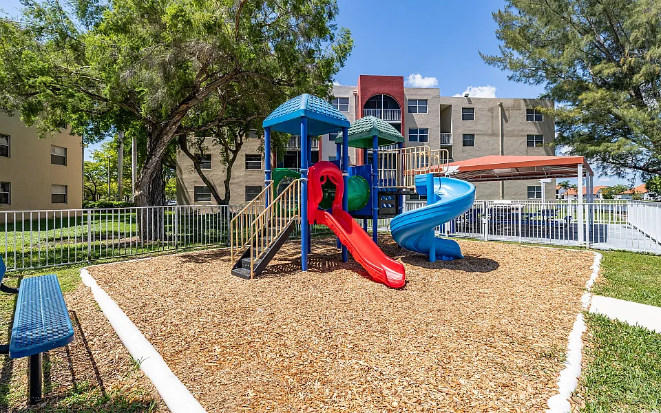 Inviting playground with colorful slides and climbing equipment, surrounded by lush greenery and modern apartment buildings.