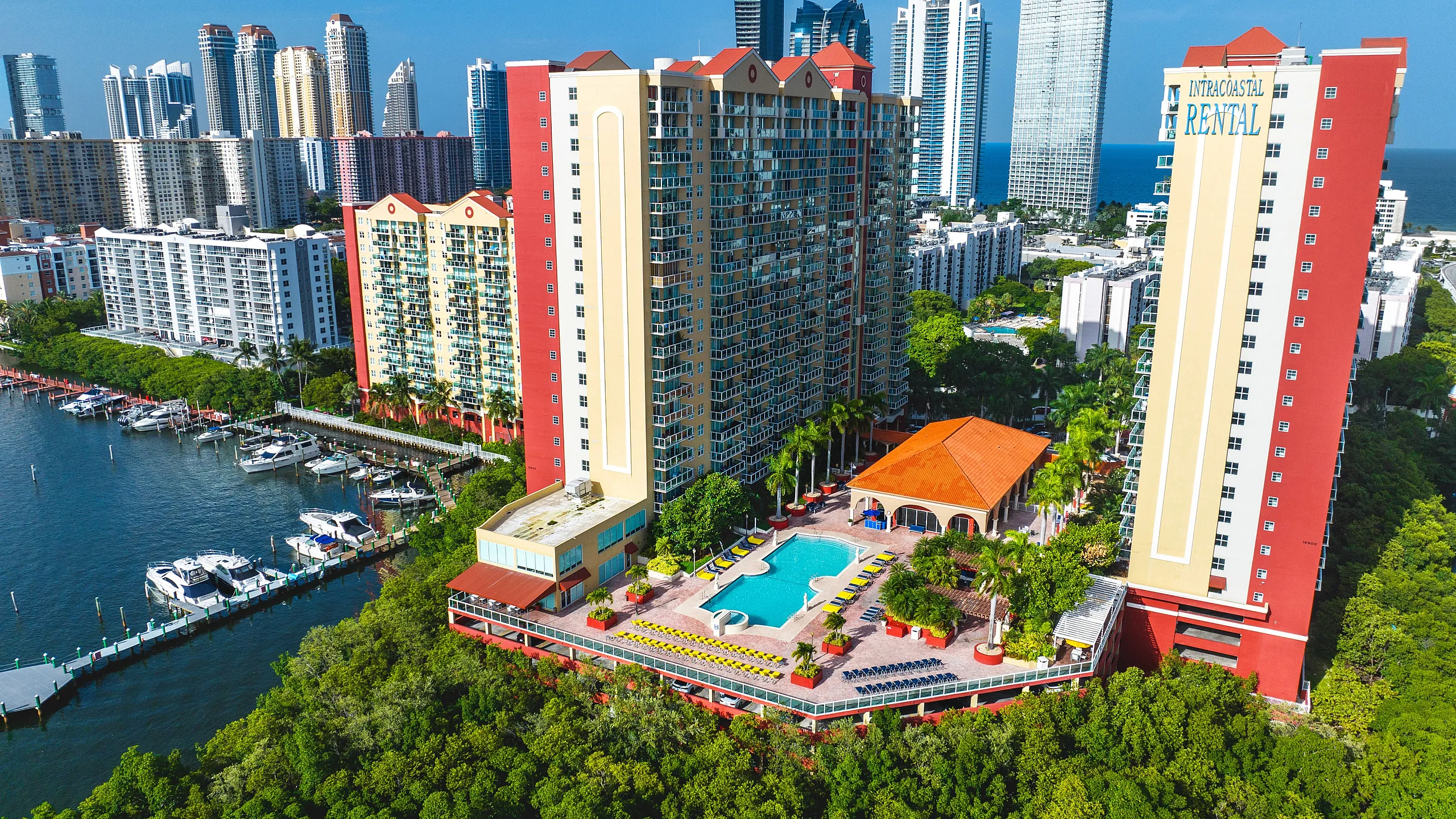 Luxurious high-rise apartment complex with stunning waterfront views, marina access, lush greenery, and a sparkling pool area in a bustling urban setting.