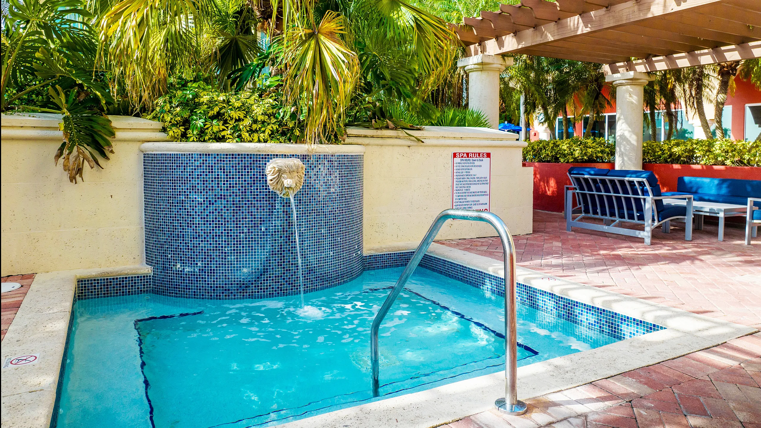 Luxurious outdoor spa area with a serene jacuzzi, surrounded by lush palms and elegant seating under a stylish pergola.