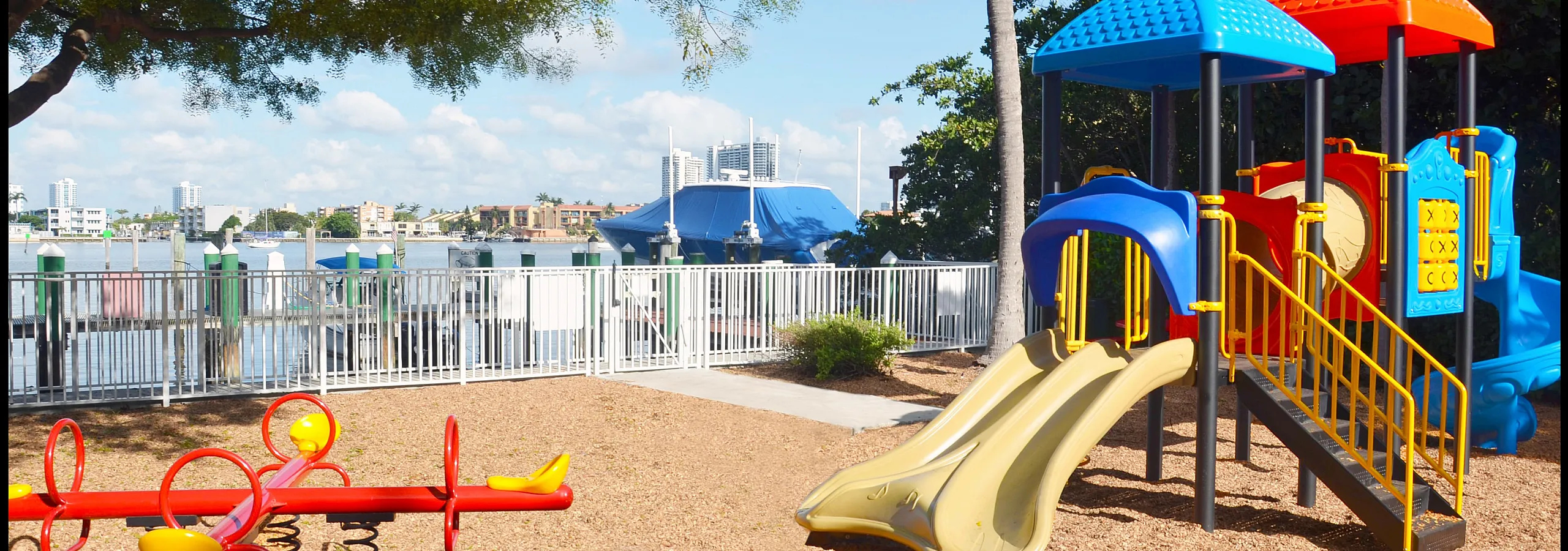 Vibrant outdoor playground with colorful slides and seesaw overlooking a serene waterfront view, perfect for family fun.