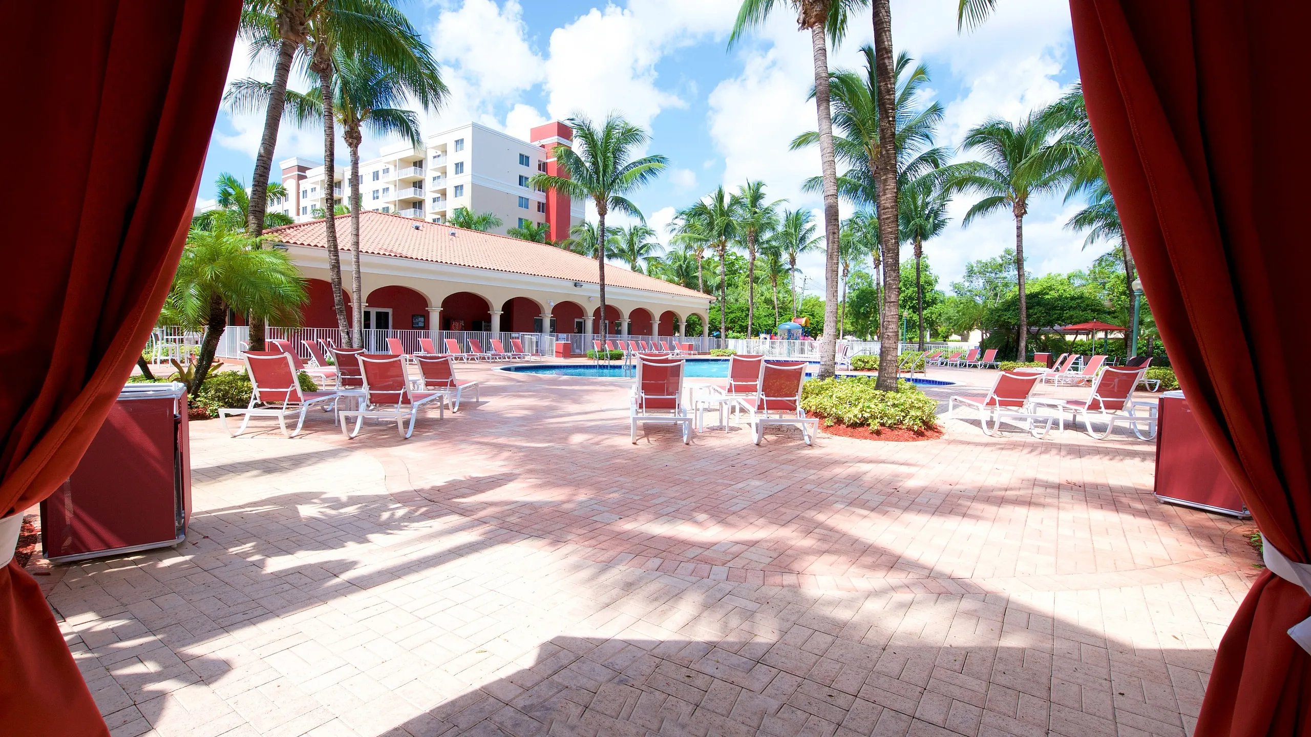 Luxurious outdoor pool area with elegant lounge chairs, surrounded by lush palm trees and modern architecture.
