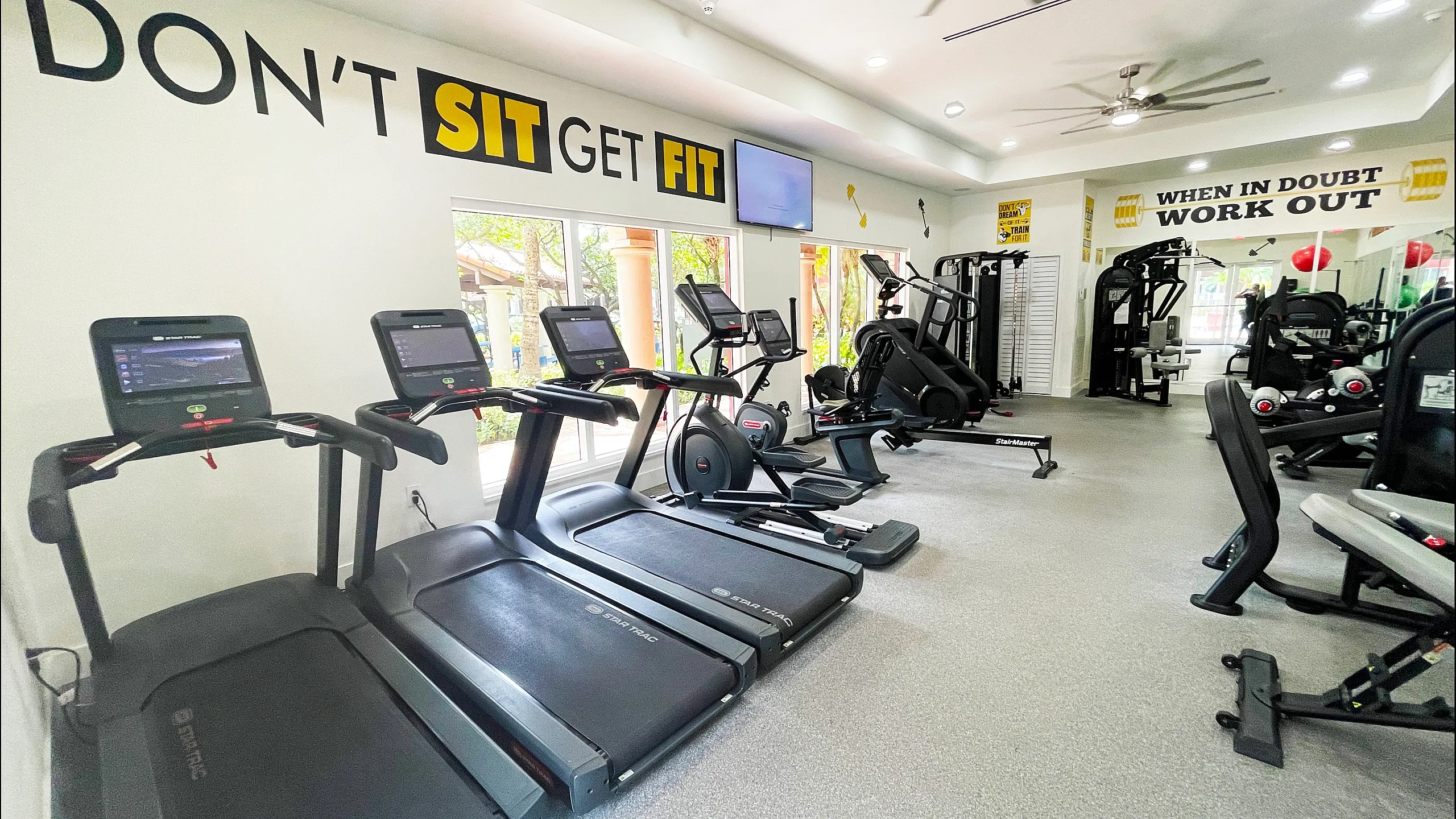 Modern fitness center featuring state-of-the-art treadmills, elliptical machines, and weightlifting equipment, highlighted by motivational wall quotes.