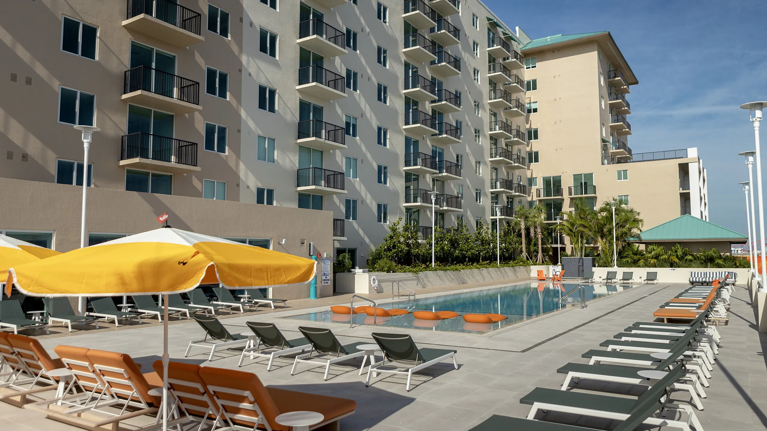 Sunlit luxury apartment complex with modern balconies, vibrant poolside lounge, and pristine swimming pool.