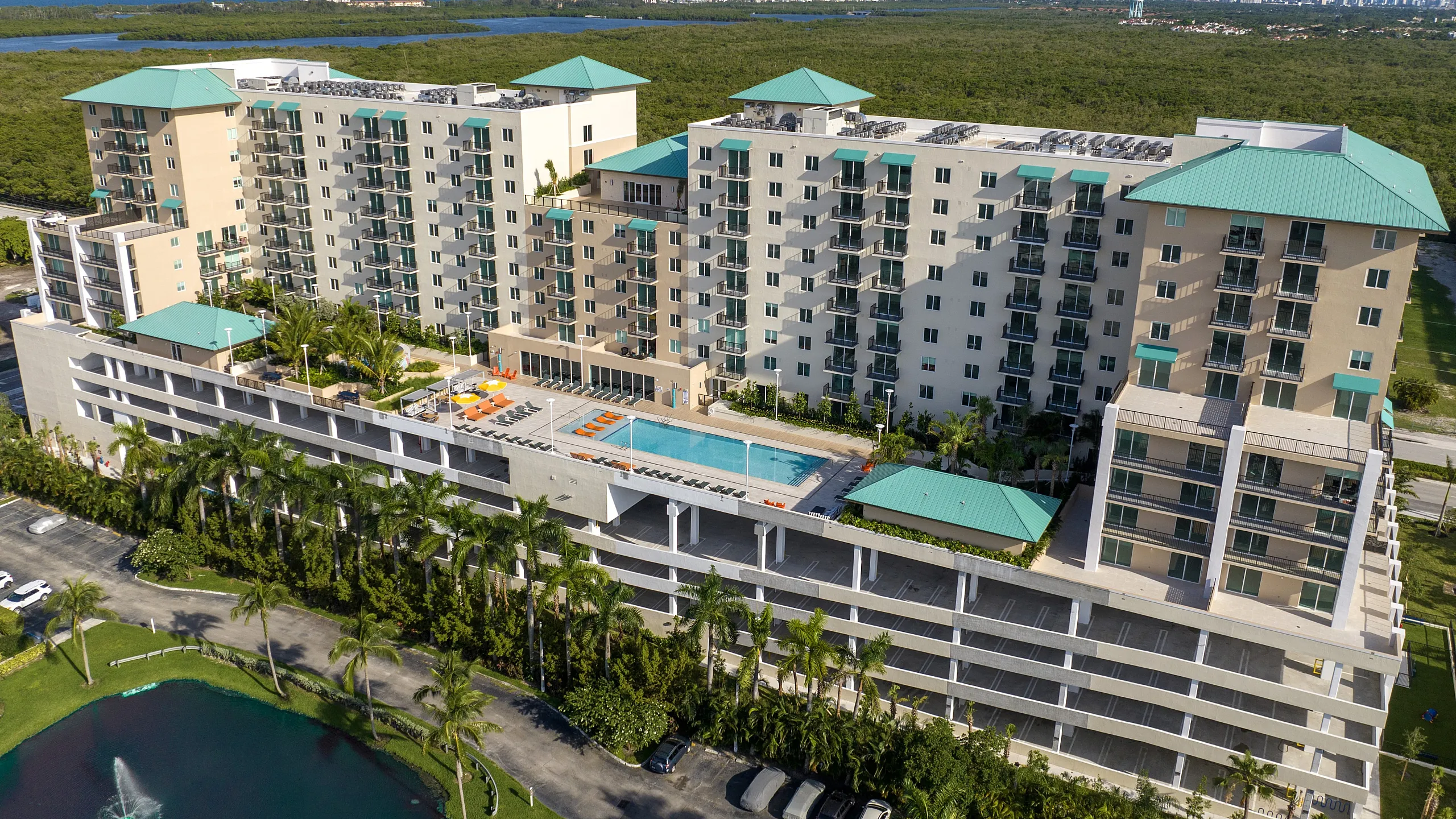 Luxurious high-rise apartment complex with turquoise rooftops, featuring a central swimming pool, surrounded by lush greenery and offering stunning panoramic views.