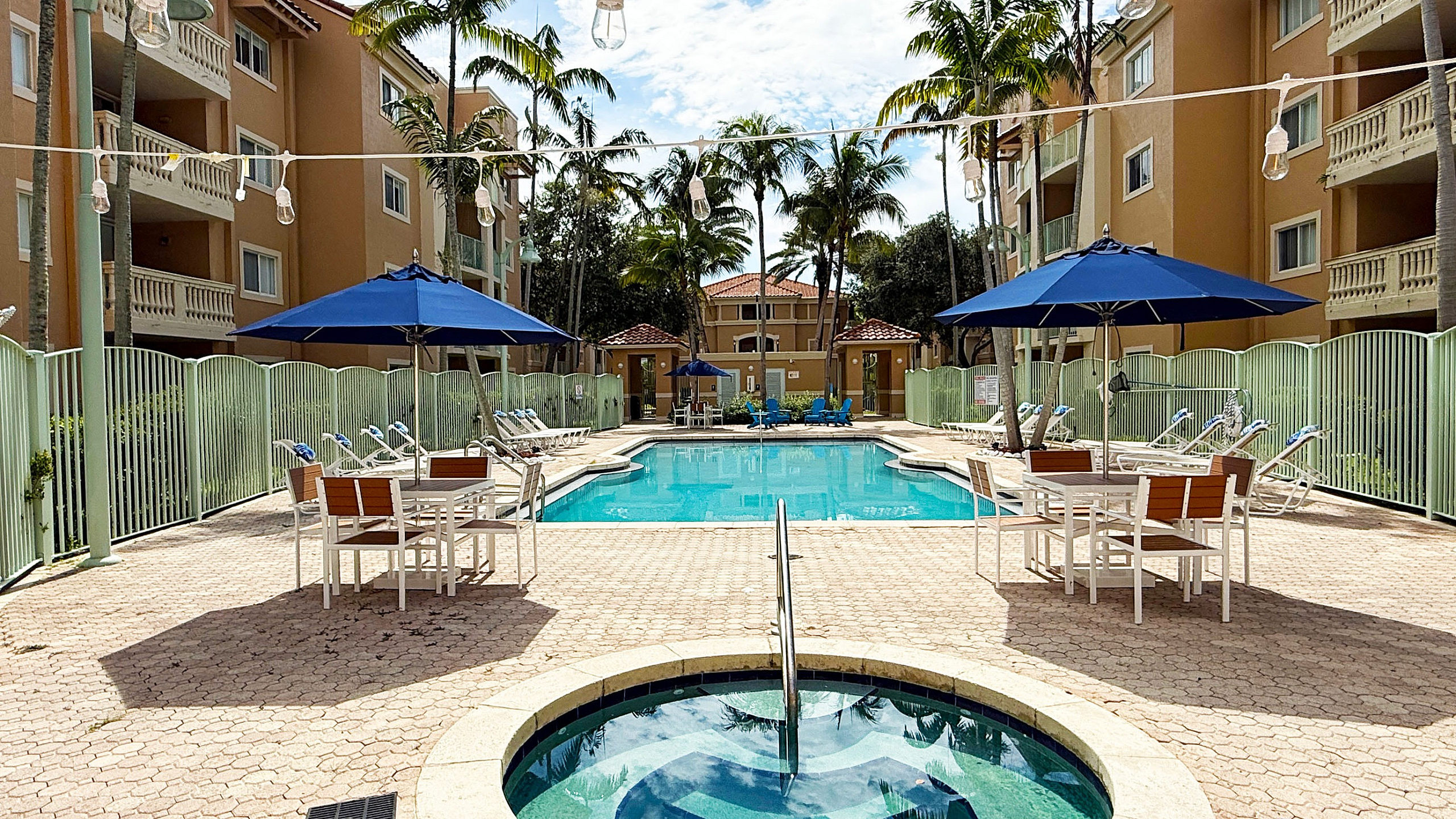 Inviting outdoor space with a stunning pool and jacuzzi, surrounded by elegant apartment buildings and lush palm trees, offering a perfect tropical retreat.