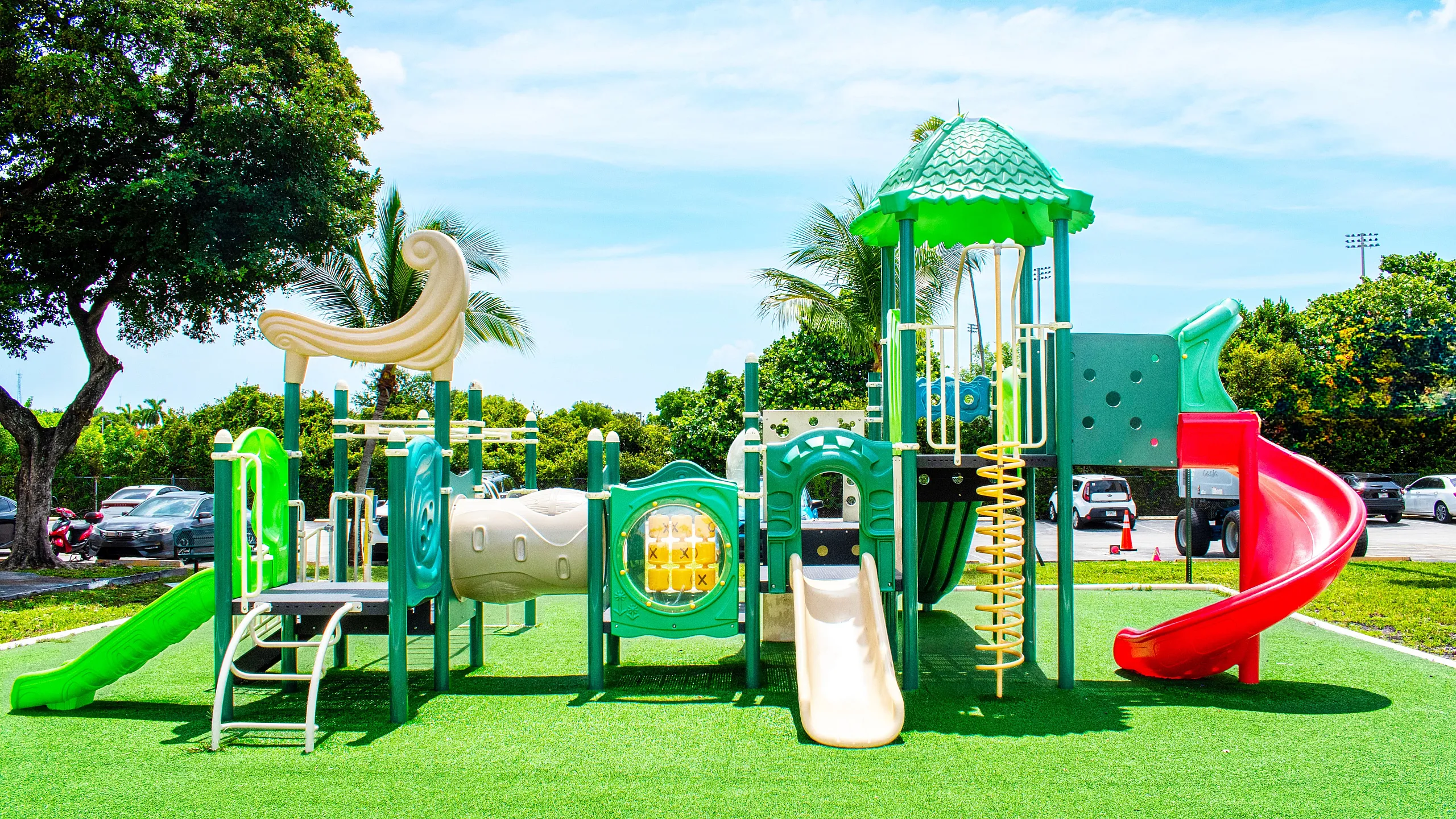 Vibrant playground with colorful slides and climbing structures, surrounded by lush greenery and a sunny sky.