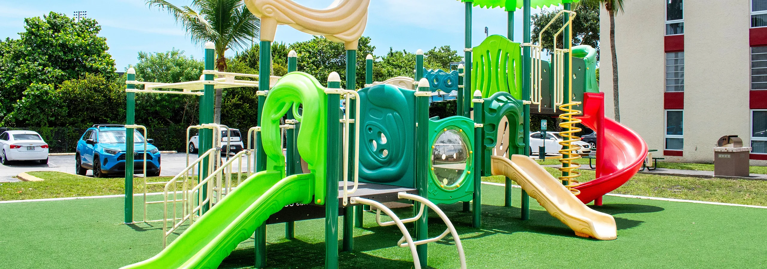 Vibrant outdoor playground featuring colorful slides and climbing structures on lush green turf, perfect for family fun in a sunny community setting.