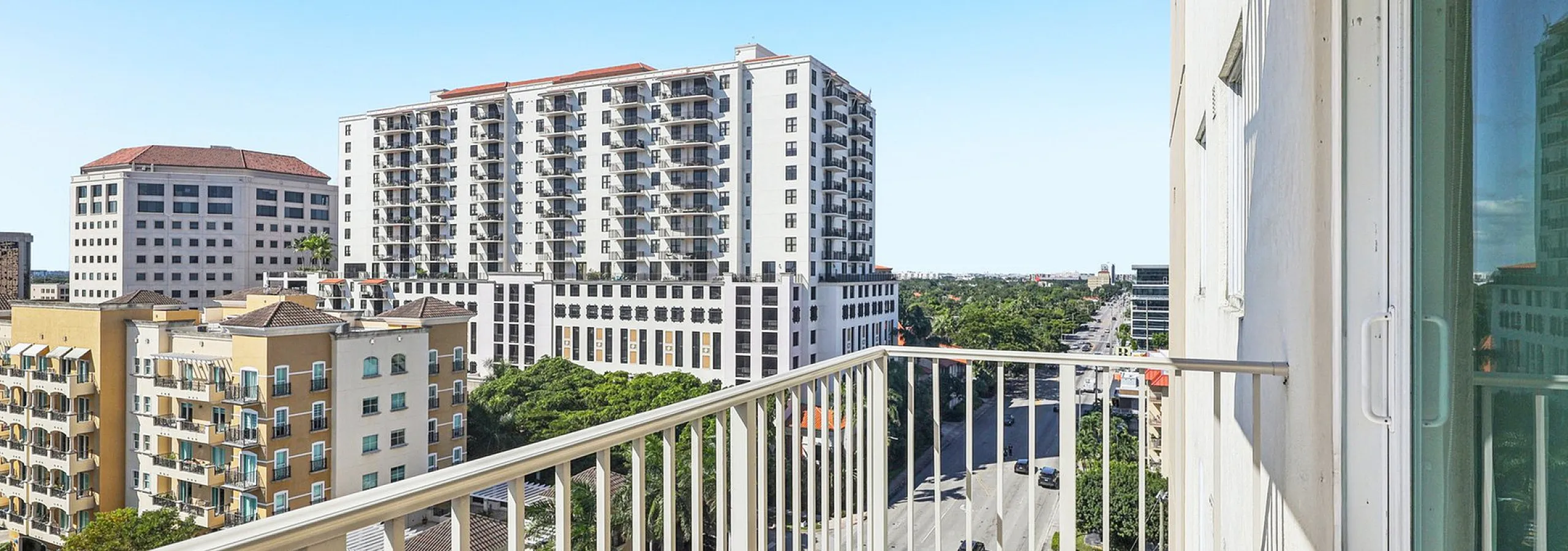 Sunlit apartment balcony with a stunning cityscape view, showcasing modern high-rise architecture and lush greenery.