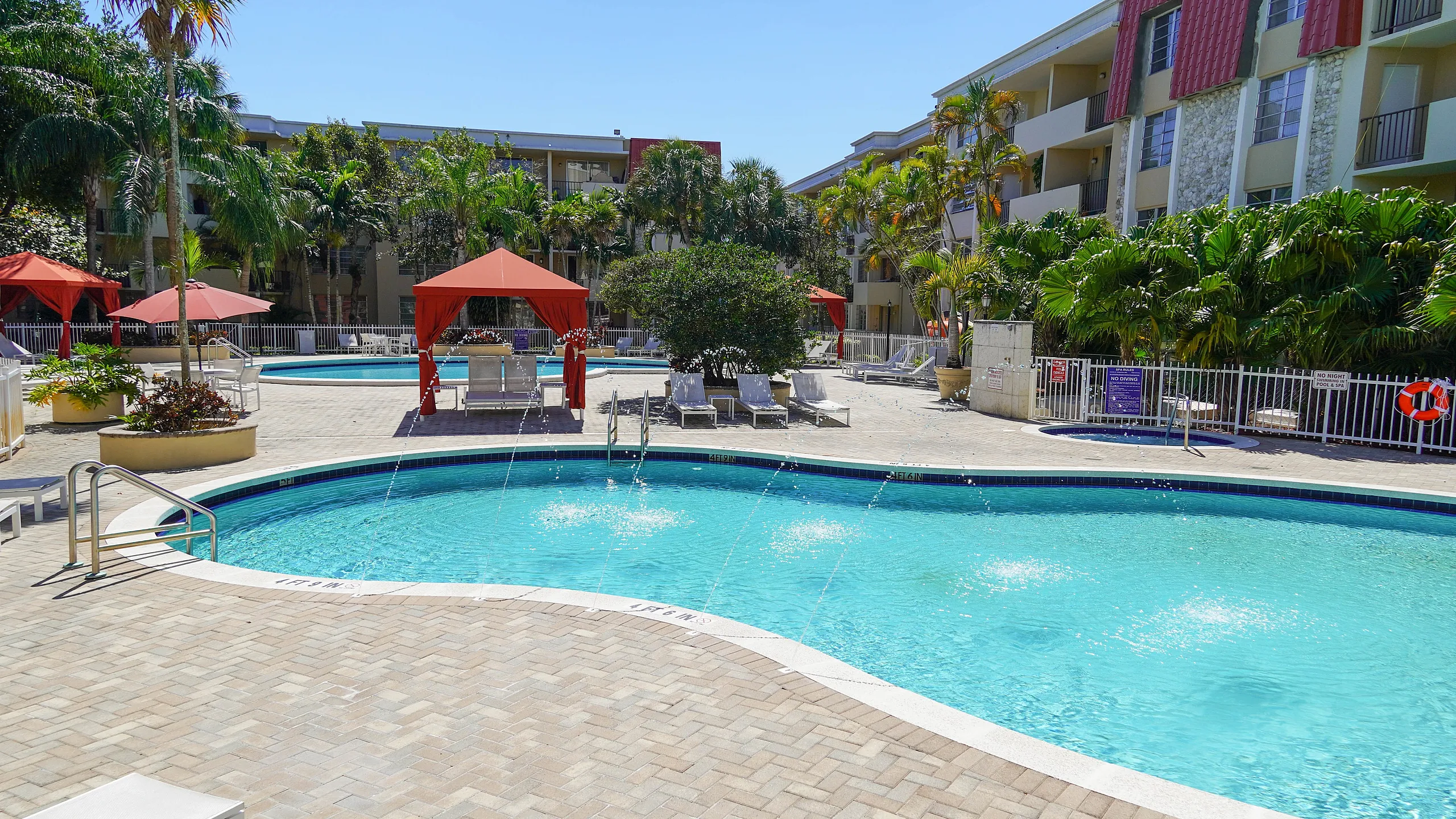 Inviting pool area featuring crystal-clear water, cozy red cabanas, and lush tropical landscaping at a stylish apartment complex.