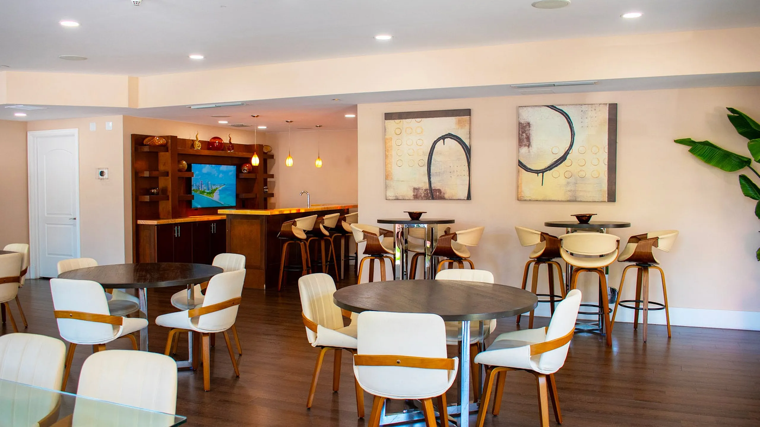Chic communal dining area with modern round tables, stylish white chairs, and a cozy bar with hanging lights and artistic wall decor.