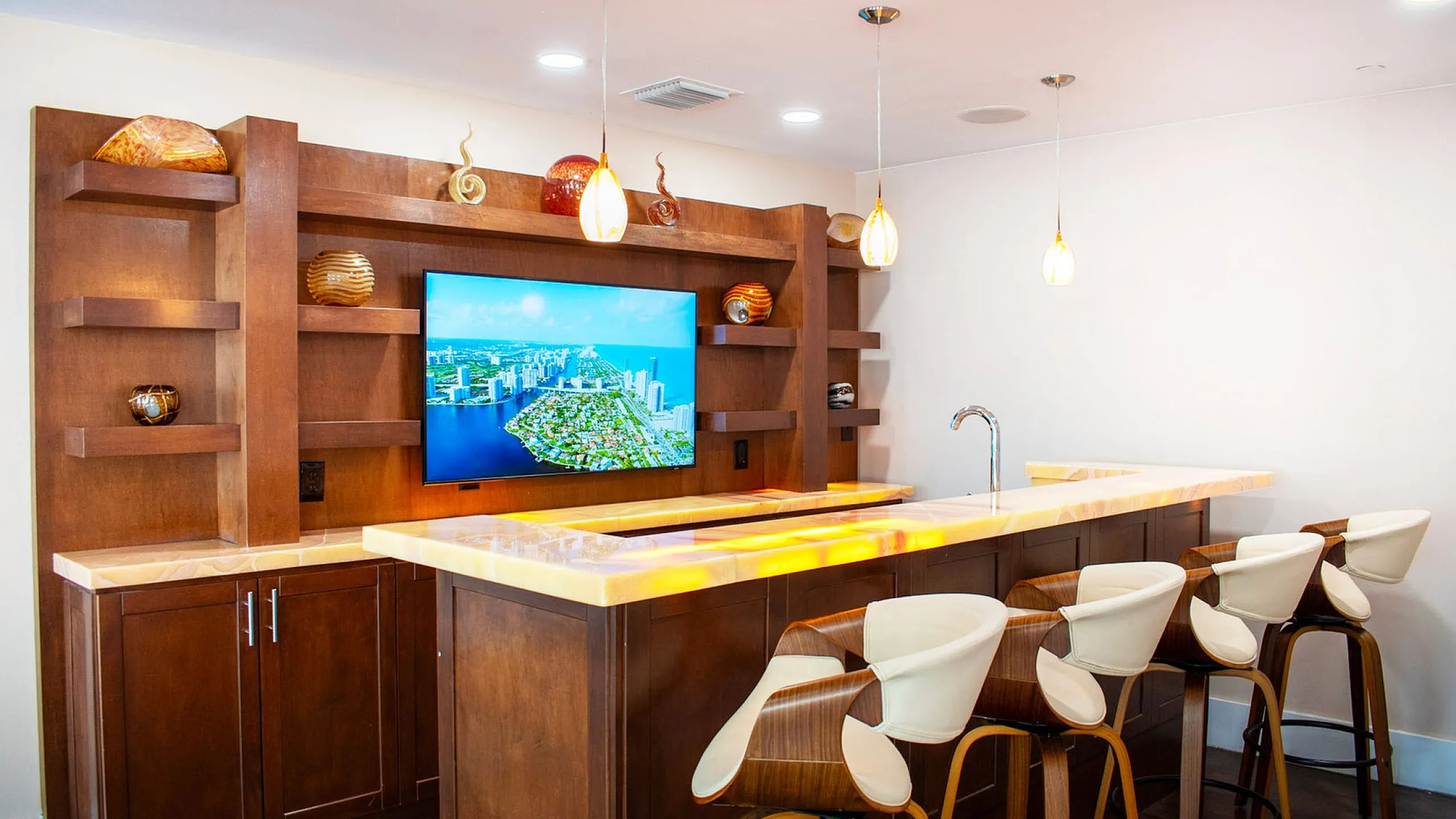 Elegant modern bar area with chic pendant lighting, illuminated countertop, and stylish wooden bar stools, ideal for entertaining.