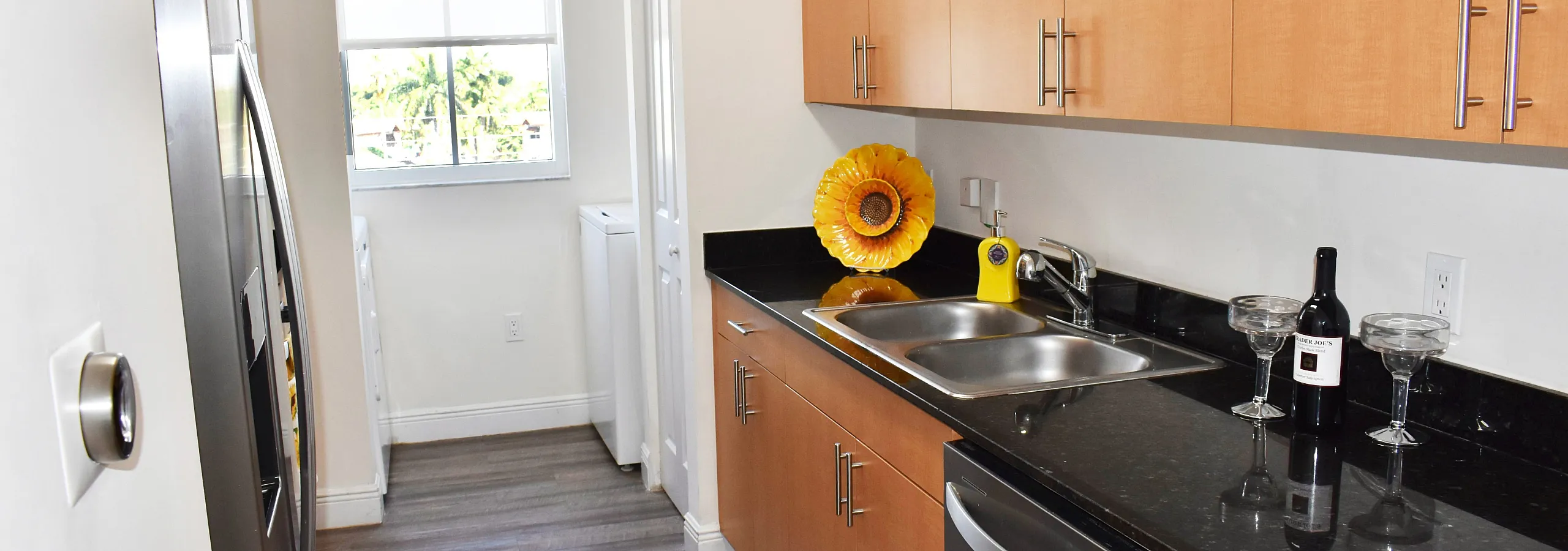 Bright and modern kitchen with sleek appliances, elegant black countertops, and natural wood cabinets, enhanced by a large window for abundant natural light.
