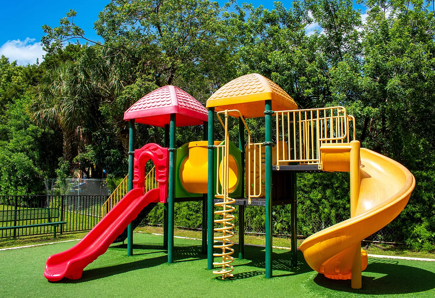 Vibrant playground featuring colorful slides and climbing structures set against lush green trees.