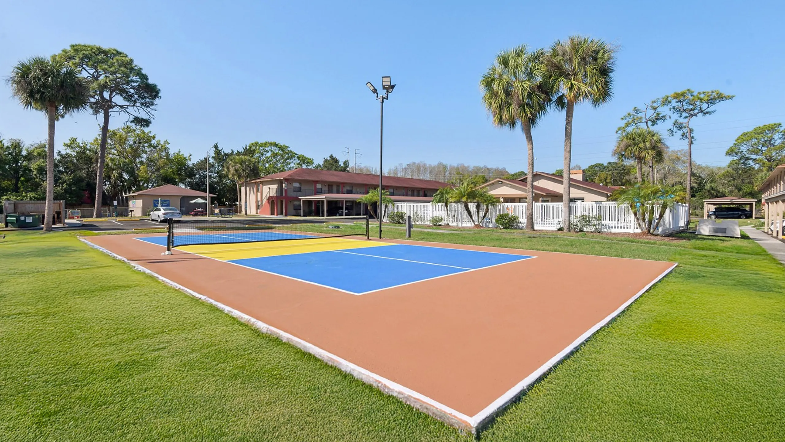 Vibrant apartment complex featuring a modern multi-sport court surrounded by lush greenery and palm trees, offering a resort-like outdoor experience.