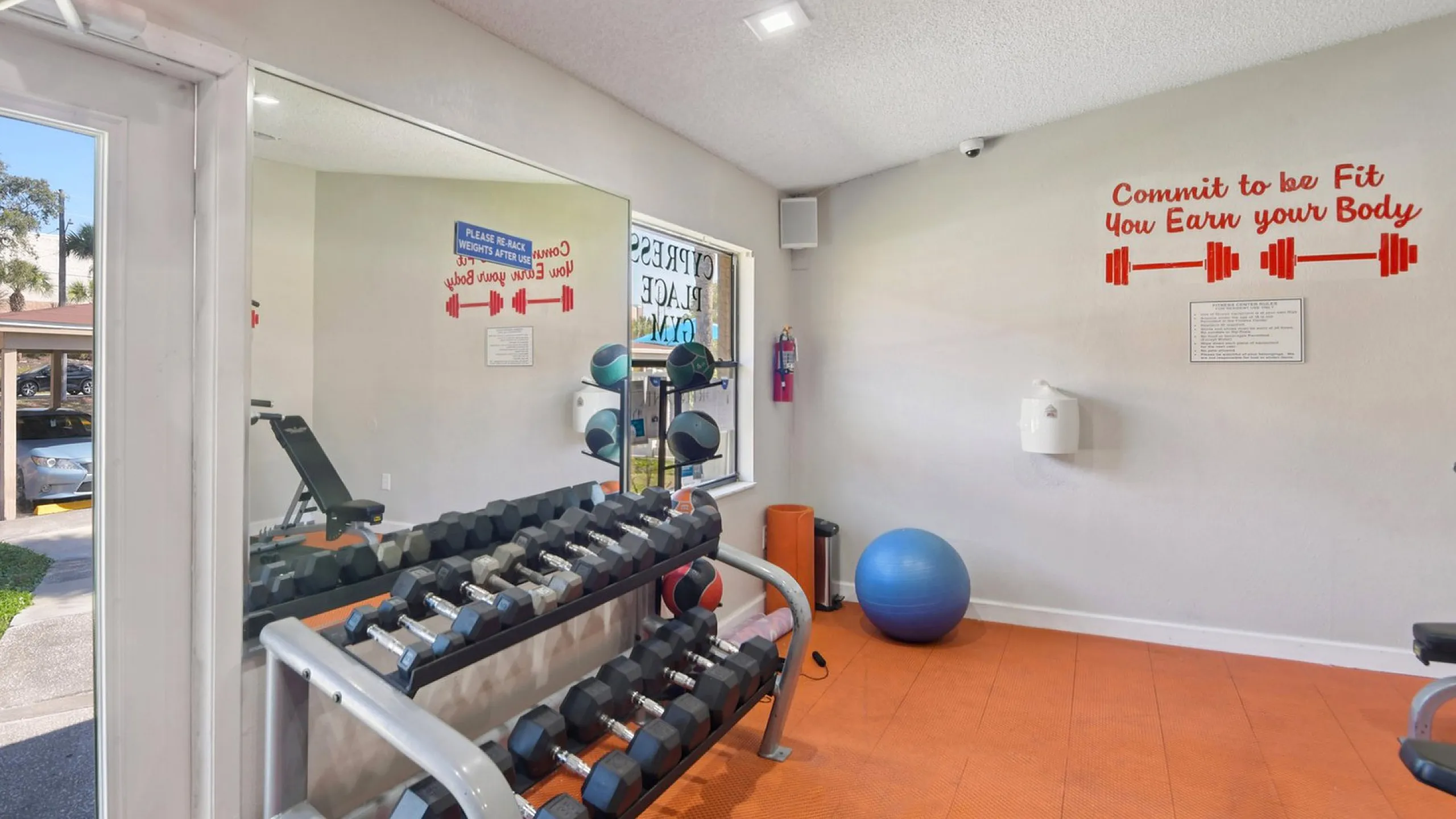 Modern fitness room with dumbbells, exercise ball, motivational decor, and large mirrors, offering a bright and energizing workout environment.