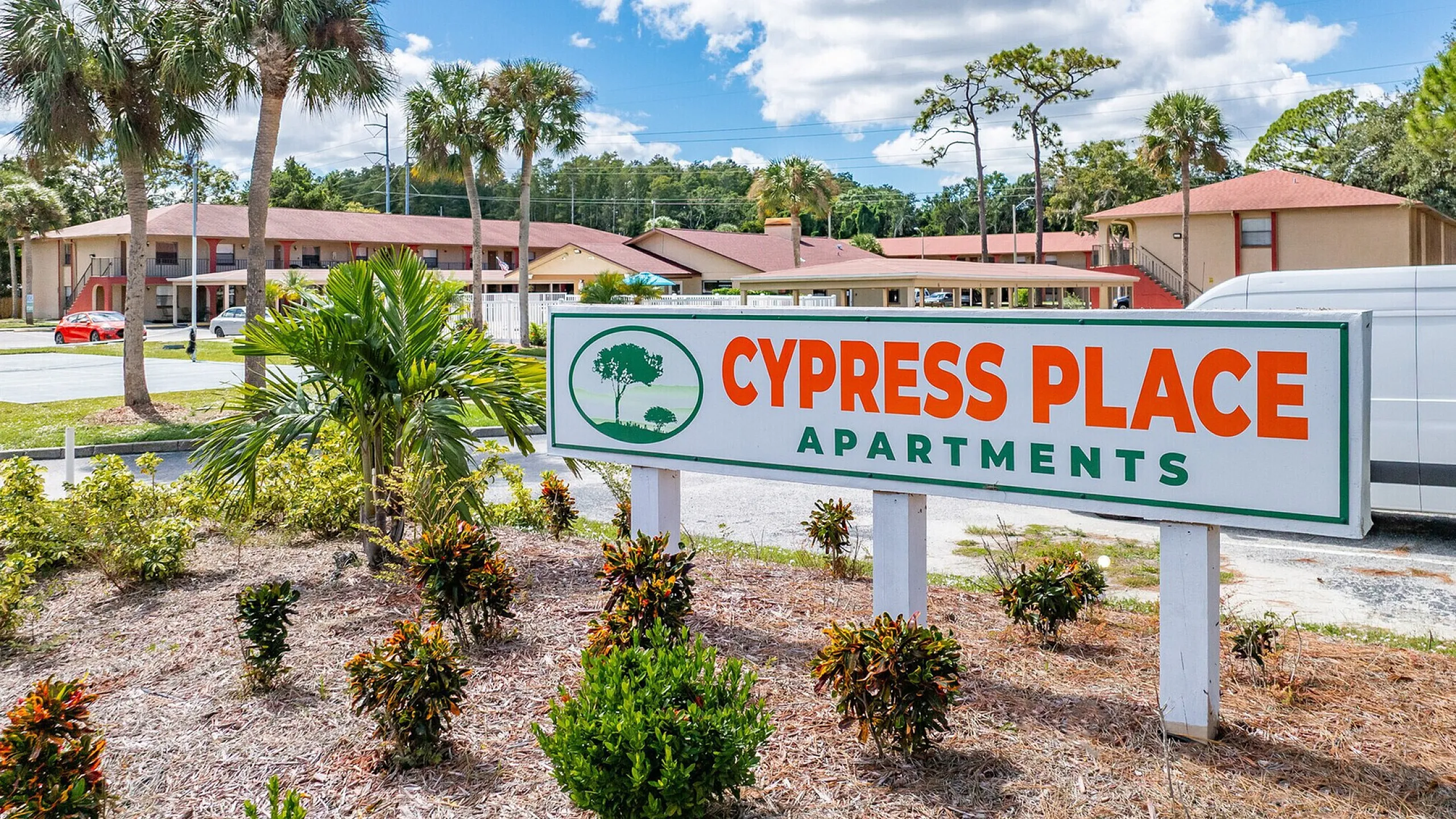 Charming Cypress Place Apartments offering serene living with lush landscaping and palm trees under a bright blue sky.