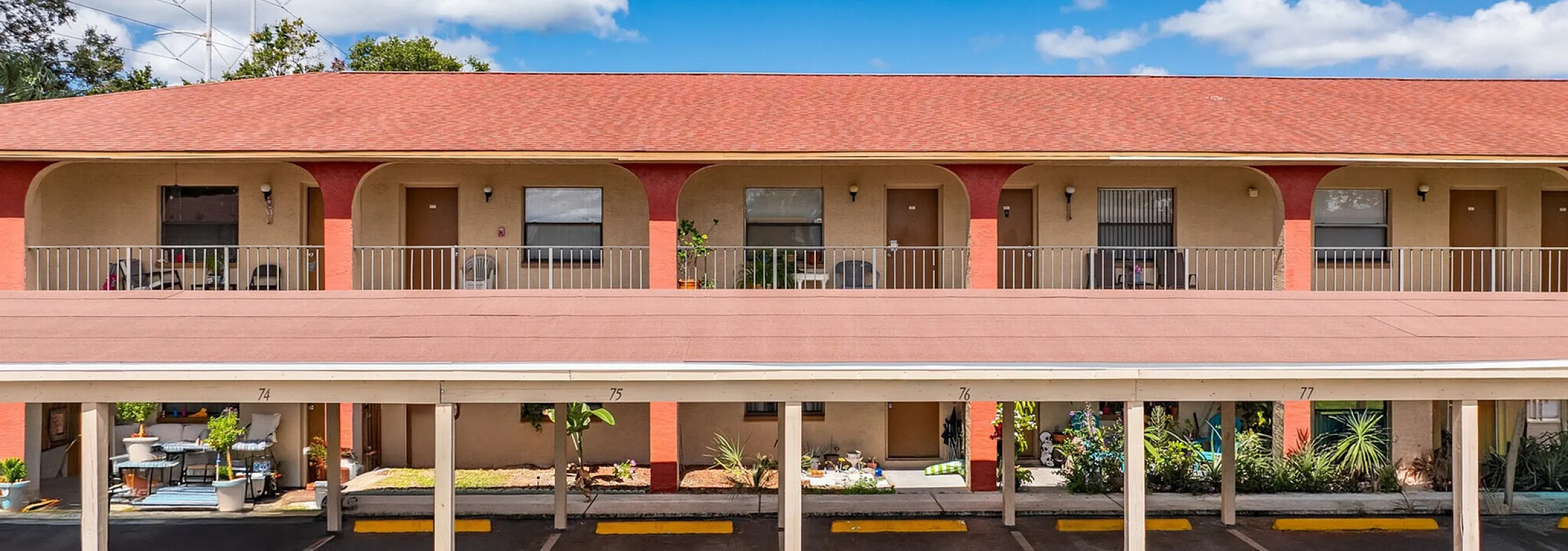 Charming apartment complex with vibrant red roofing, picturesque balconies, and lush greenery under a bright blue sky.