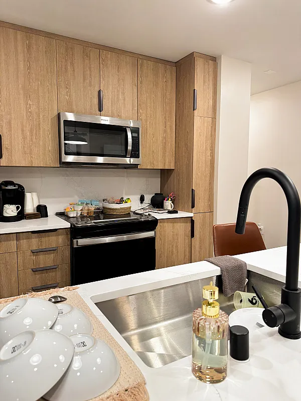 Kitchen sink up close, kitchen cabinets, oven, stove, and microwave in the background