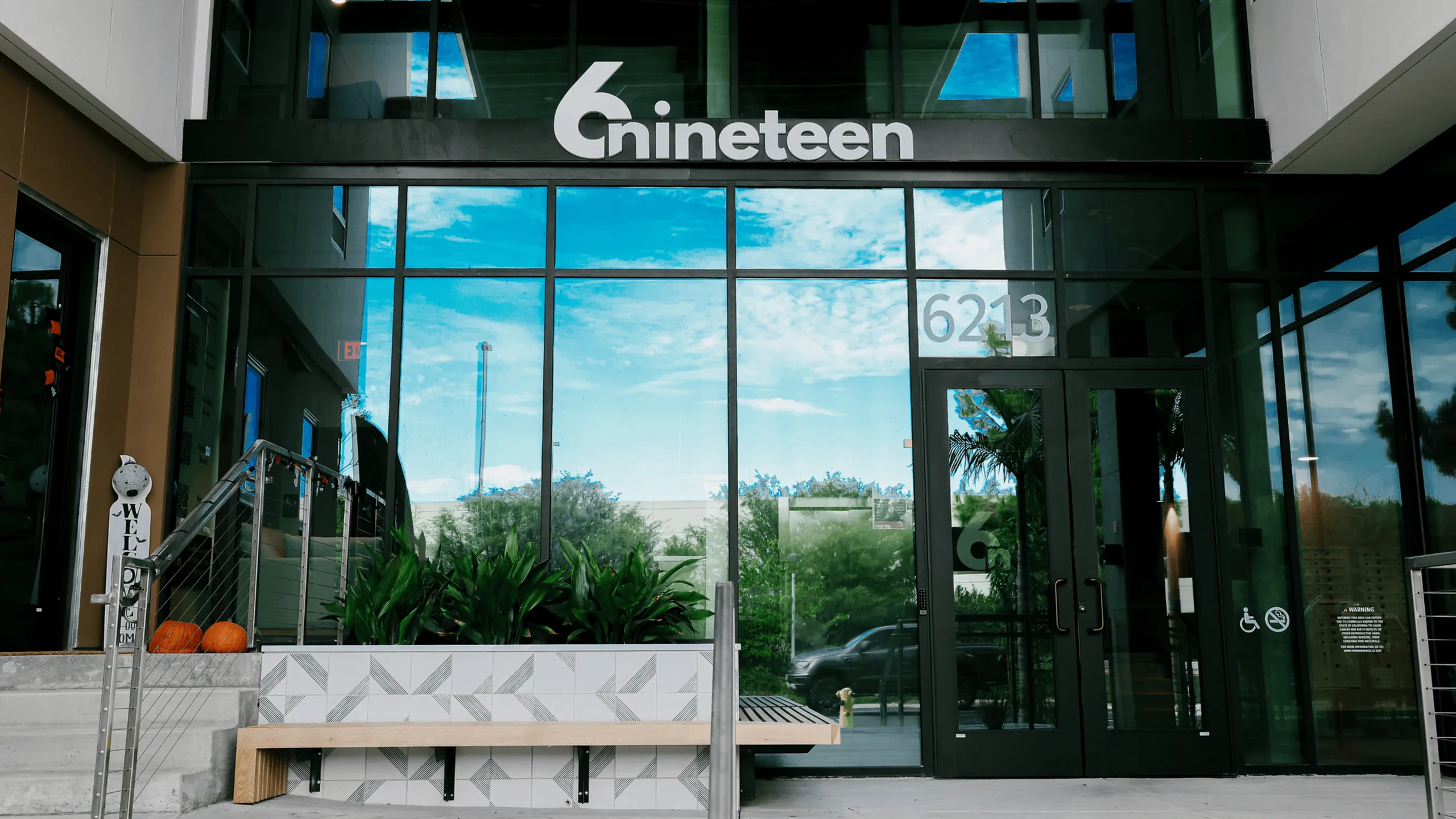 The front entrance of 6Nineteen in San Diego displays the building&rsquo;s modern glass fa&ccedil;ade and landscaped seating area, welcoming residents and visitors.