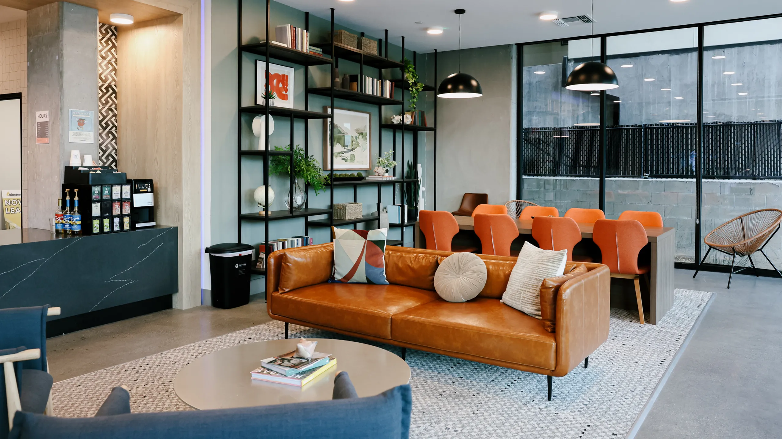 A vibrant common area at 6Nineteen in San Diego highlights lounge seating, a long study table with orange chairs, and built-in shelving, creating an inviting space for work or relaxation.