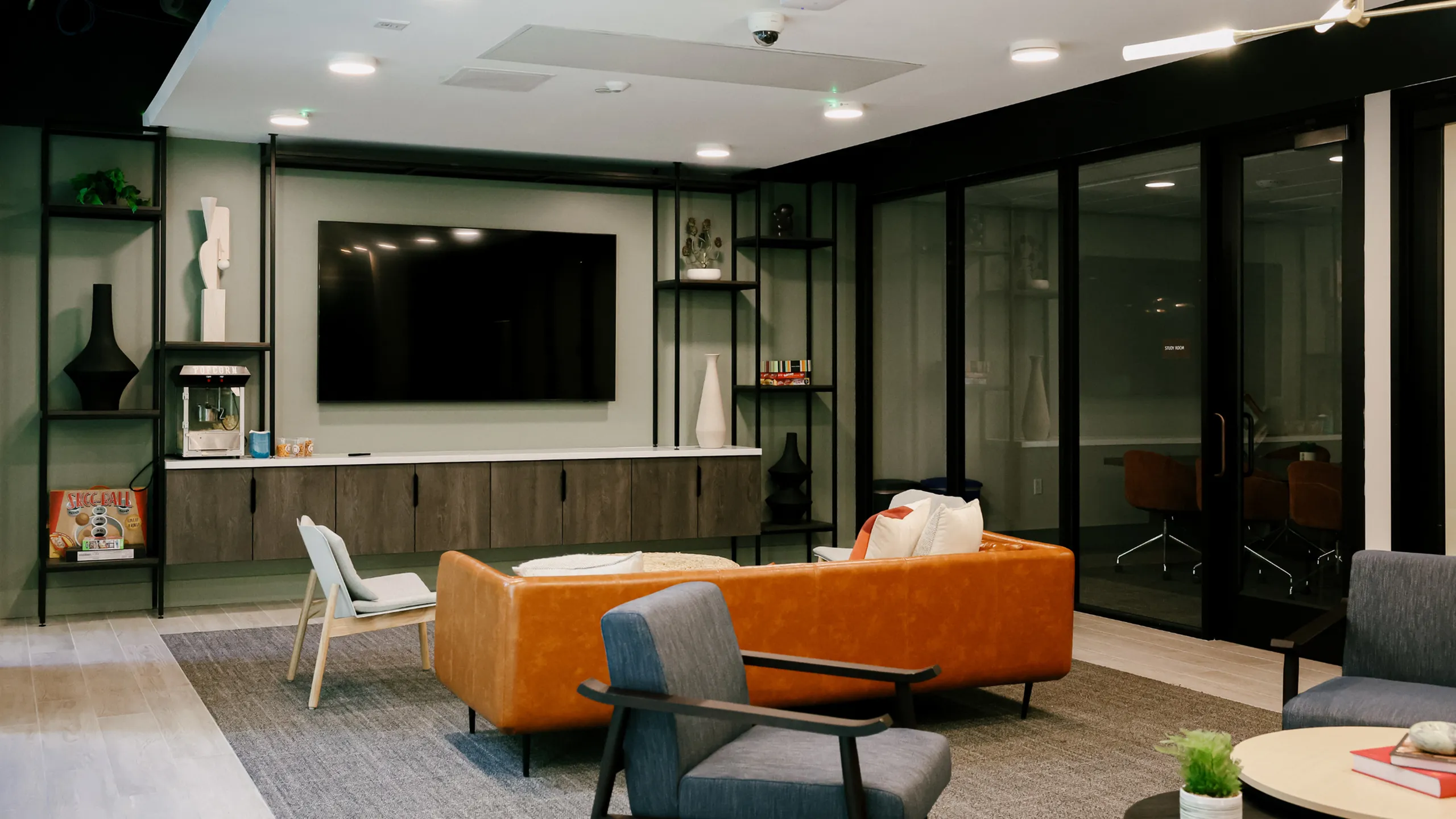 A stylish resident lounge at 6Nineteen in San Diego showcases a cozy seating area with a leather sofa, a large TV, and built-in shelving for a relaxing social space.