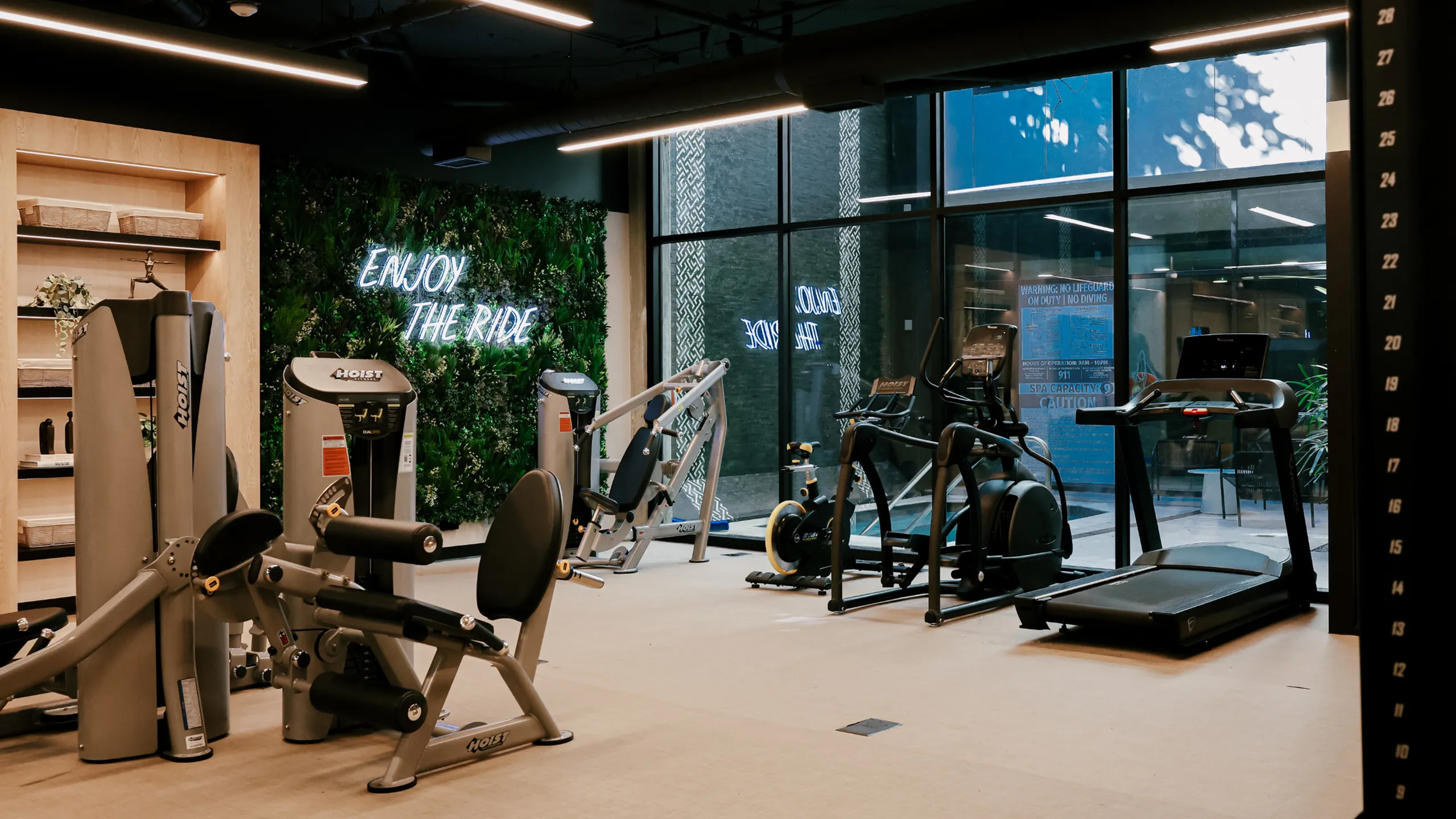The 6Nineteen fitness center in San Diego includes premium strength and cardio equipment set against a living-green accent wall with a glowing &ldquo;Enjoy the Ride&rdquo; sign.