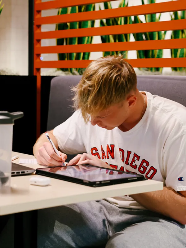 A student works on a tablet at a clean, modern study lounge table, showcasing the quiet workspaces available in this student housing community.