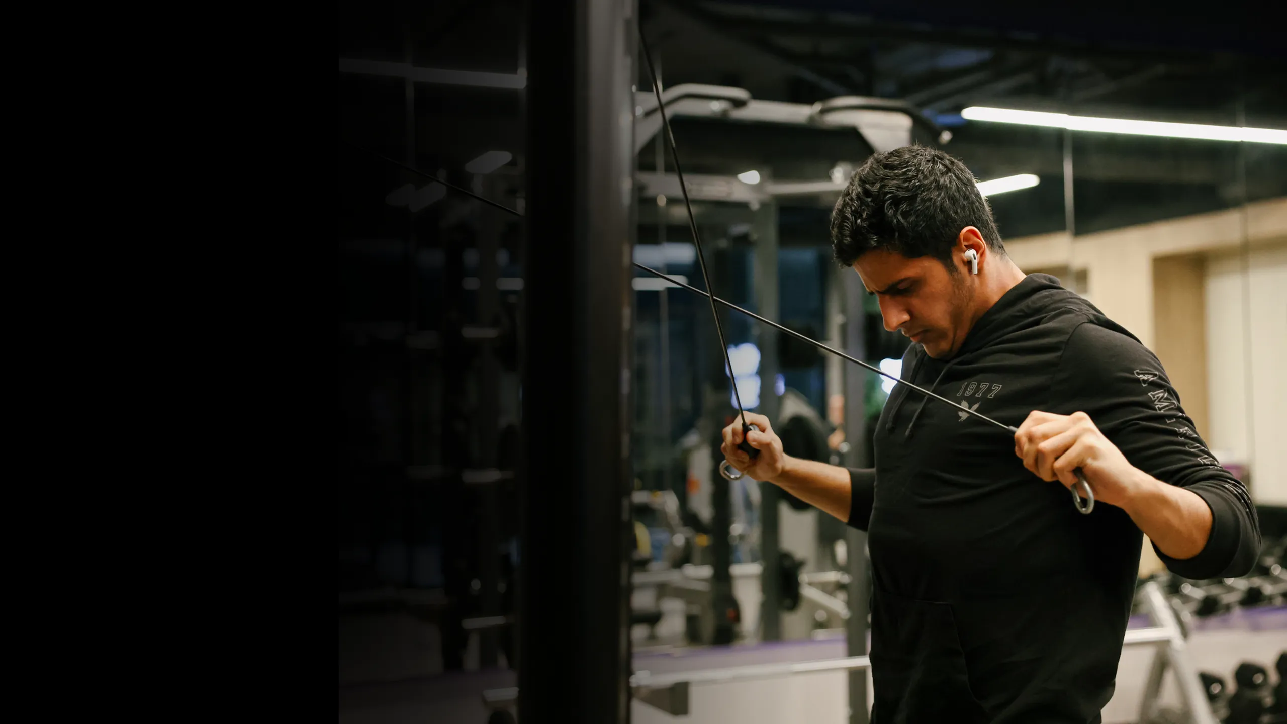 Resident working out on a cable machine in a modern apartment fitness center with strength equipment and sleek lighting, showcasing the on-site gym amenities designed for convenient, active living.