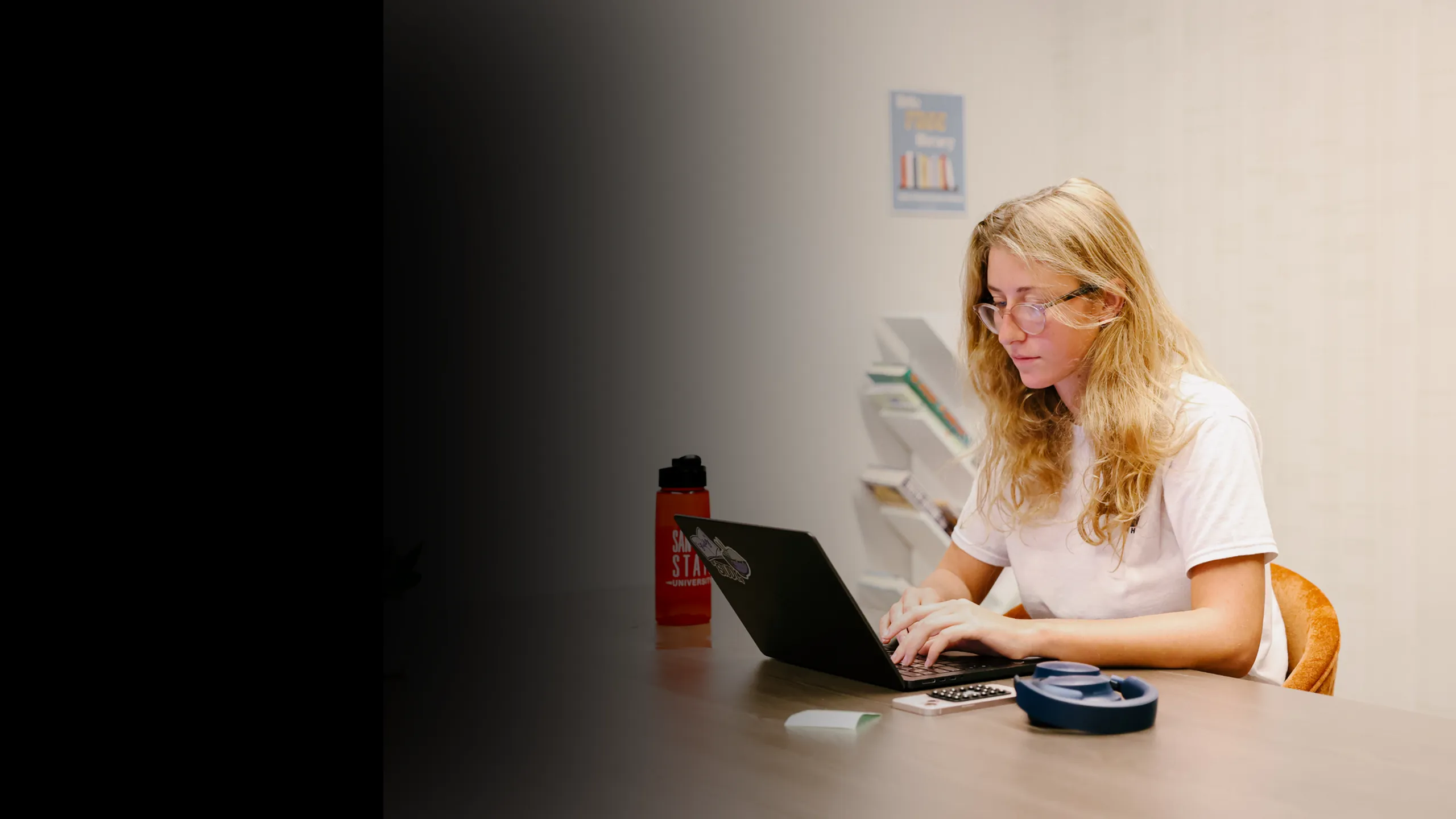Student working on a laptop at a table in a quiet apartment community study room, featuring comfortable seating and a focused environment ideal for student living.