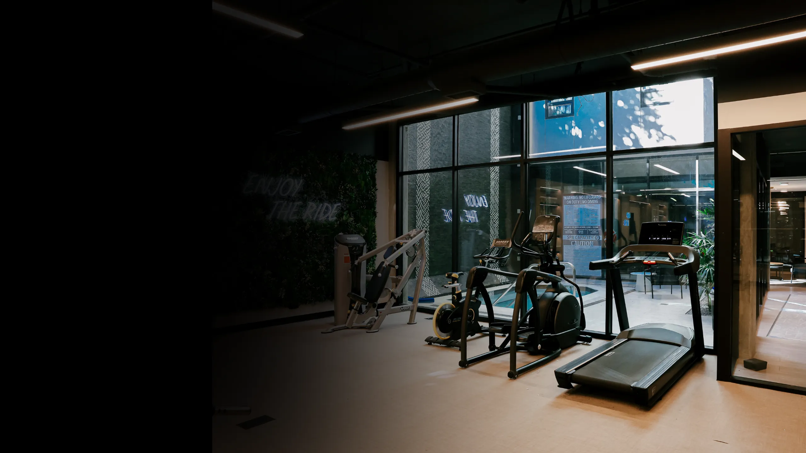 Modern apartment fitness center with treadmills, stationary bikes, strength equipment, and floor-to-ceiling windows bringing in natural light, offering residents a convenient on-site gym for everyday workouts.