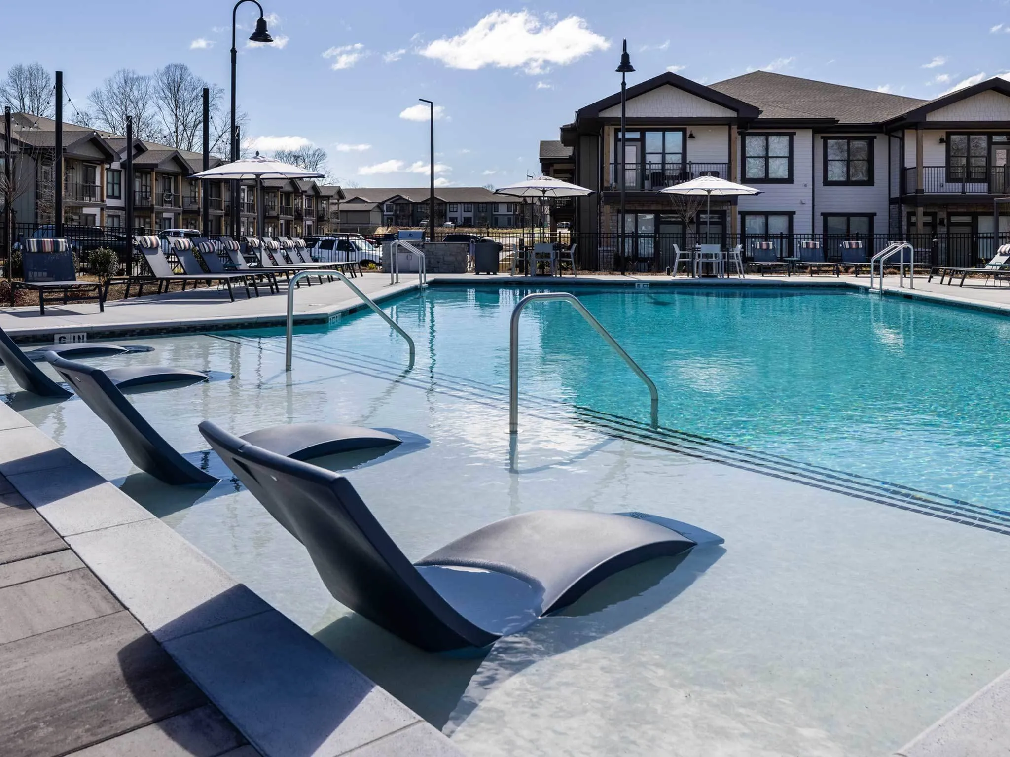 Large and shimmering pool with lounge chairs, and sun-bathing space