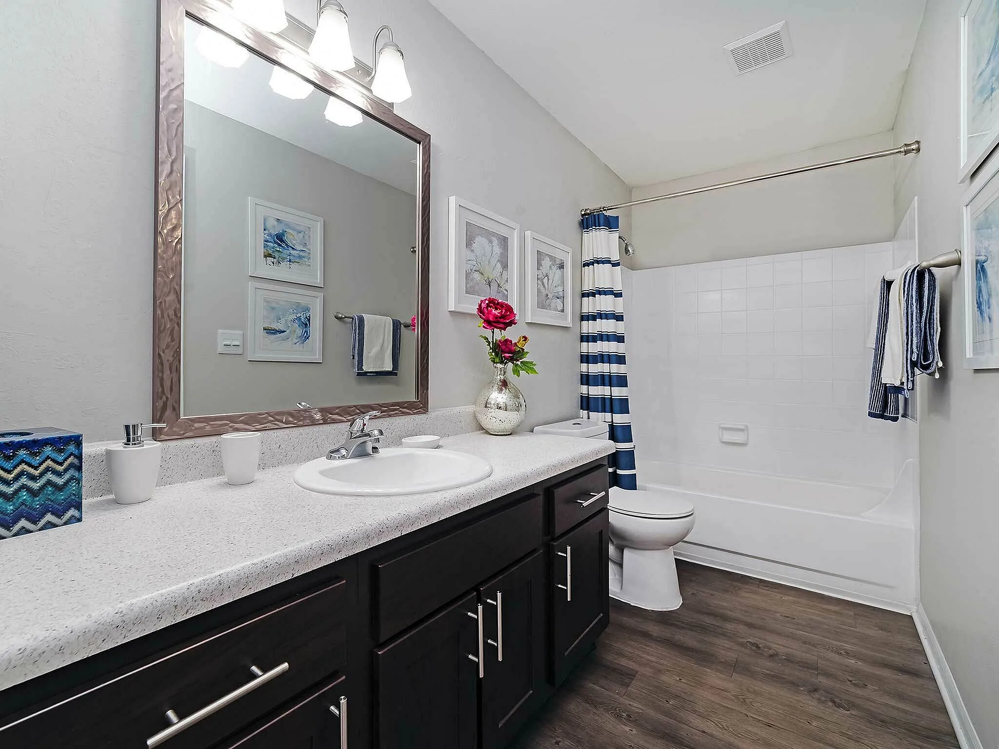 Chic bathroom with sleek dark cabinets, a large mirror, and stylish decor including a flower vase.