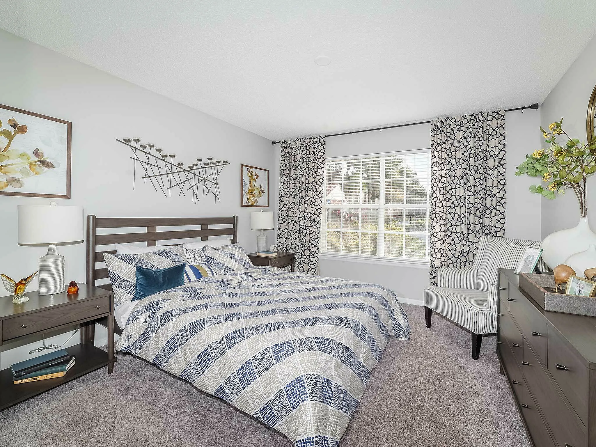 Bright and inviting bedroom with elegant decor, featuring a modern bed, stylish side tables, and a large window with patterned drapes.