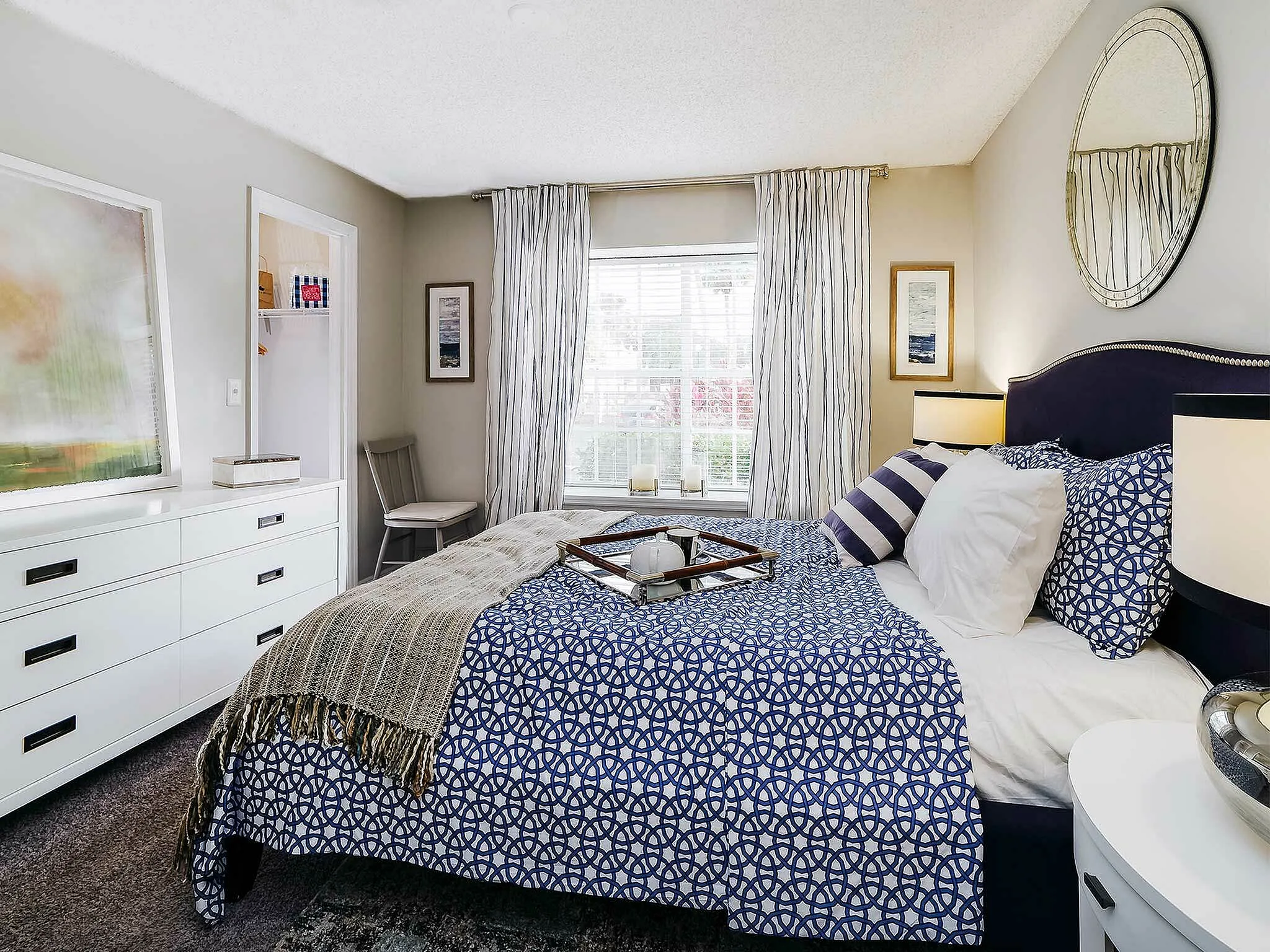 Inviting bedroom with modern decor, featuring a stylish bed with patterned blue bedding, elegant white furniture, and natural light.