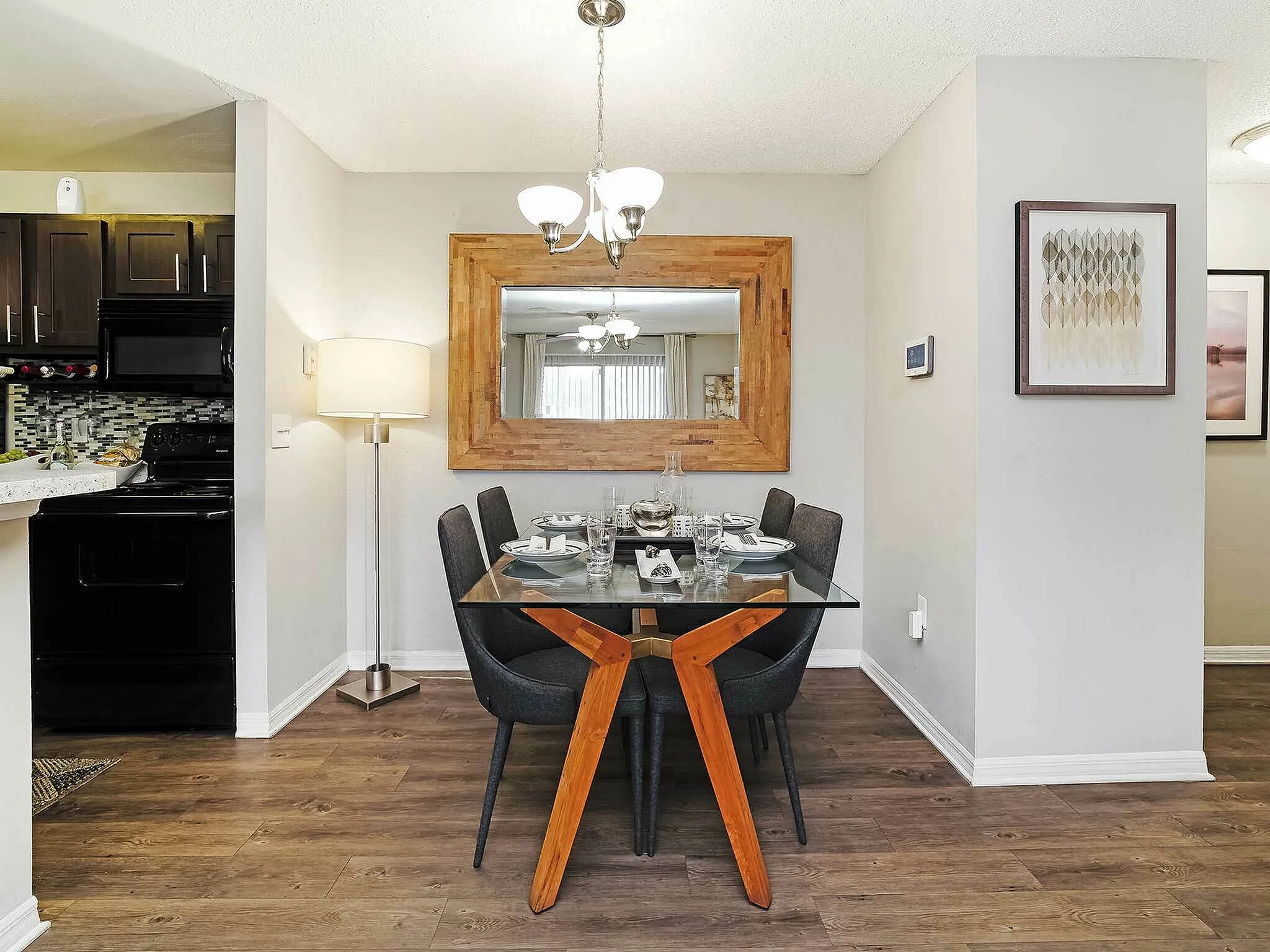 Stylishly set dining area with a glass table and dark chairs, adjacent to a modern kitchen.