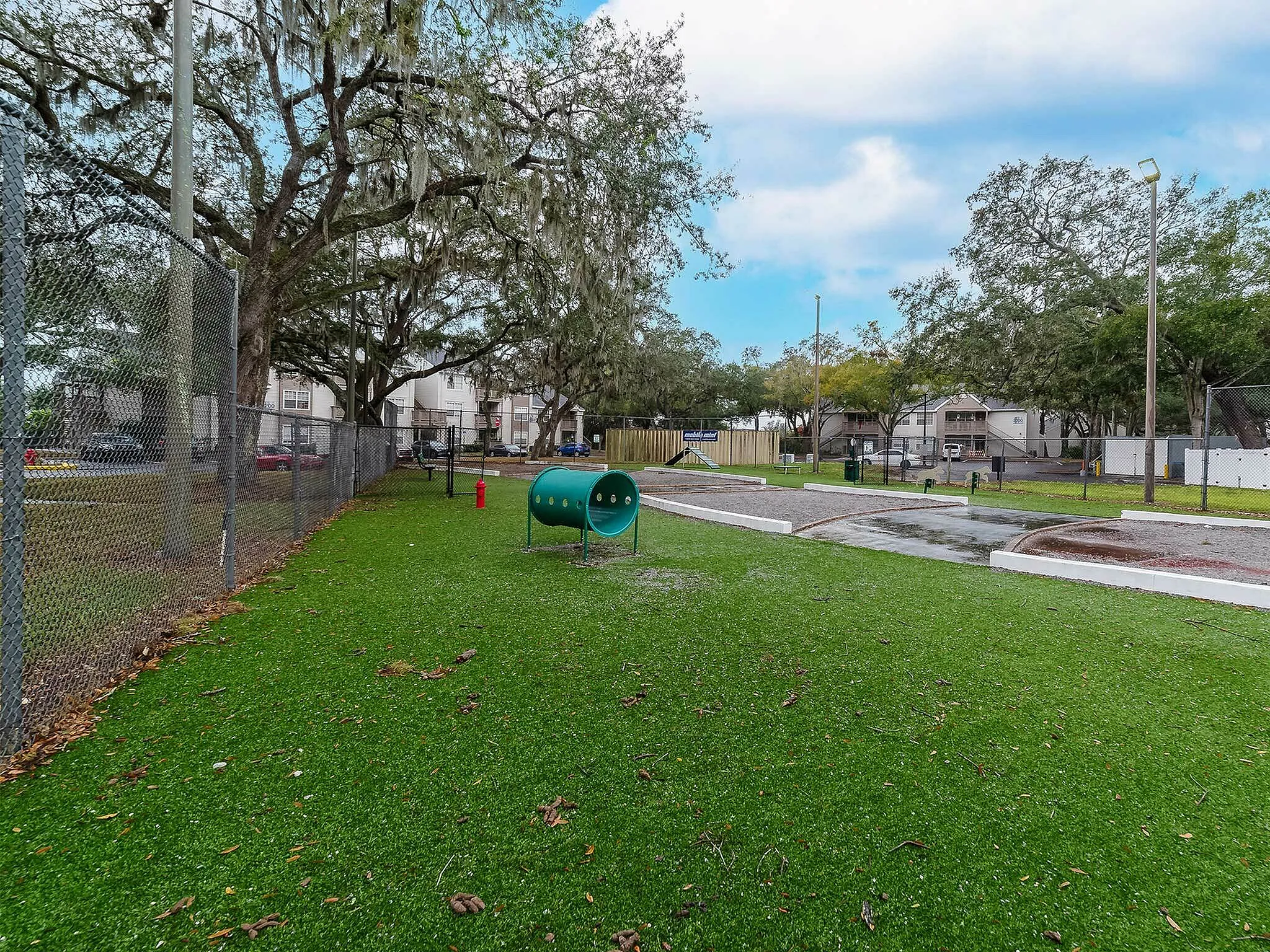 Inviting dog park with lush greenery, dog play equipment, and surrounding mature trees.