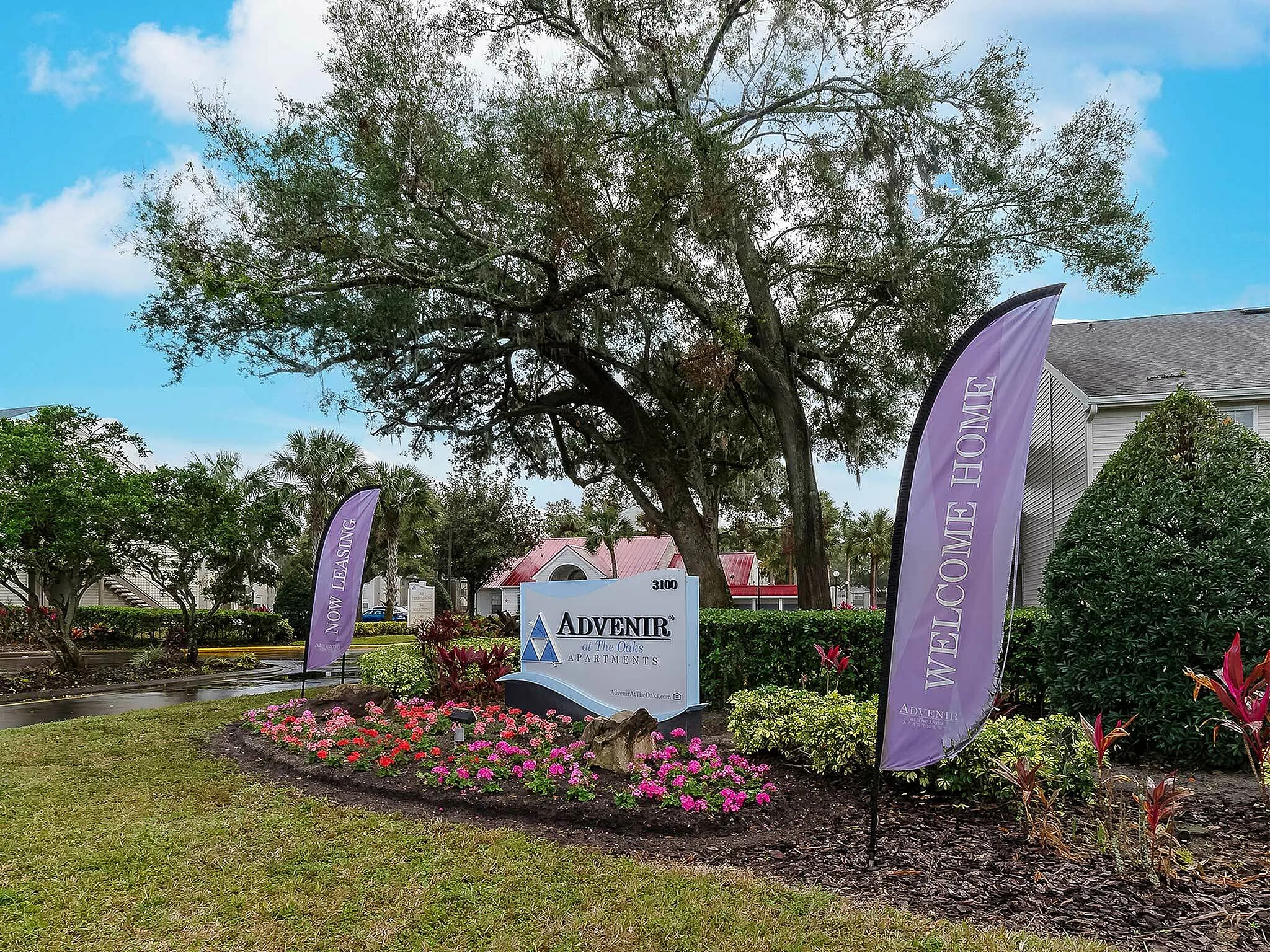 Charming entrance to Advenir at The Oaks Apartments with lush landscaping and welcoming banners.