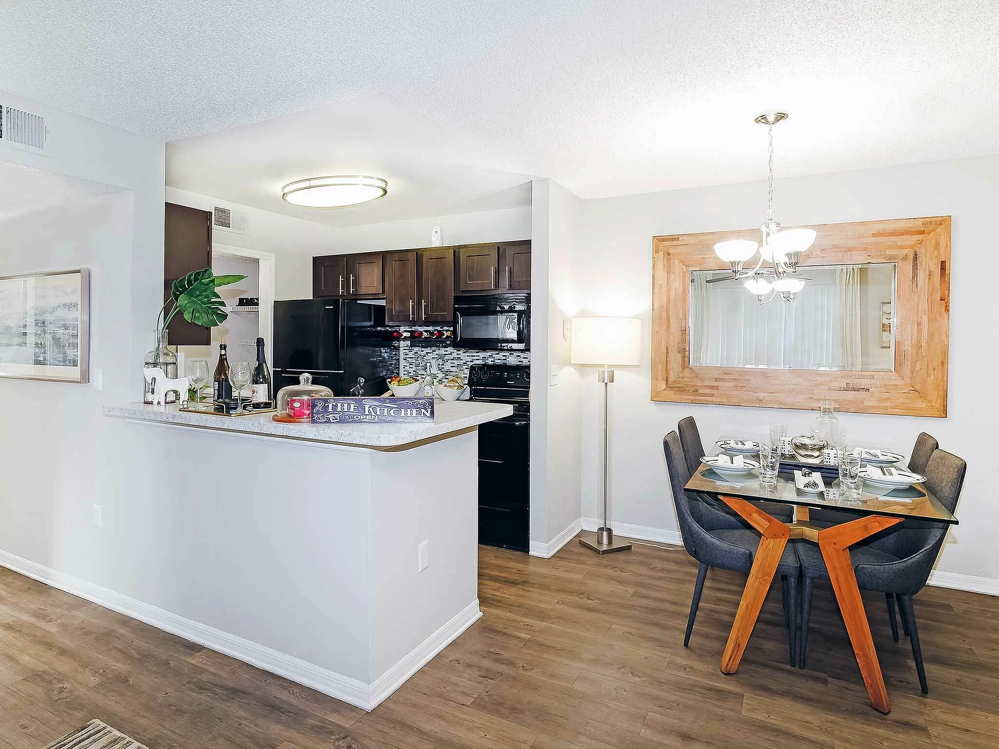 Bright dining space with a glass table and modern kitchen featuring dark cabinetry and stylish decor.