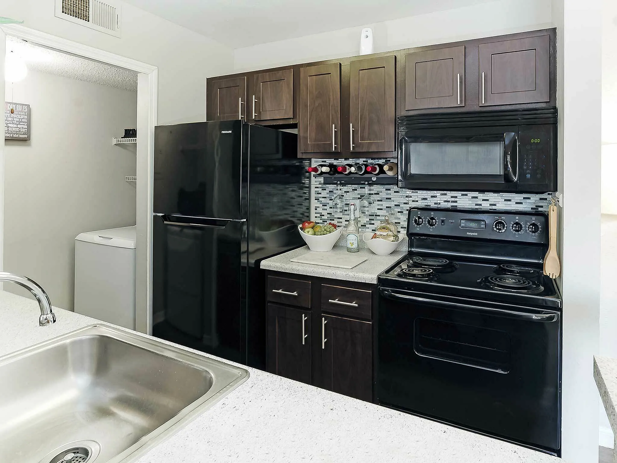 Modern kitchen with dark cabinetry, sleek black appliances, and a mosaic tile backsplash.