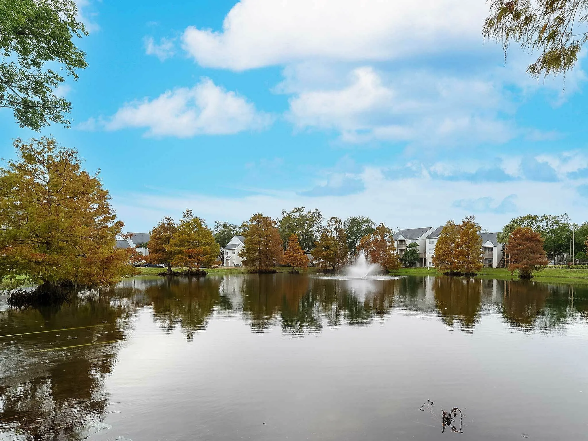 Beautiful lake view with autumn trees and elegant apartments under a vibrant blue sky.
