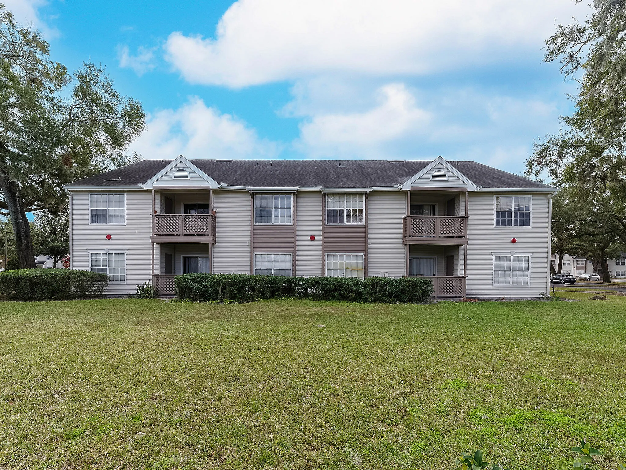Elegant two-story apartment building with charming balconies, surrounded by lush greenery and open lawns.