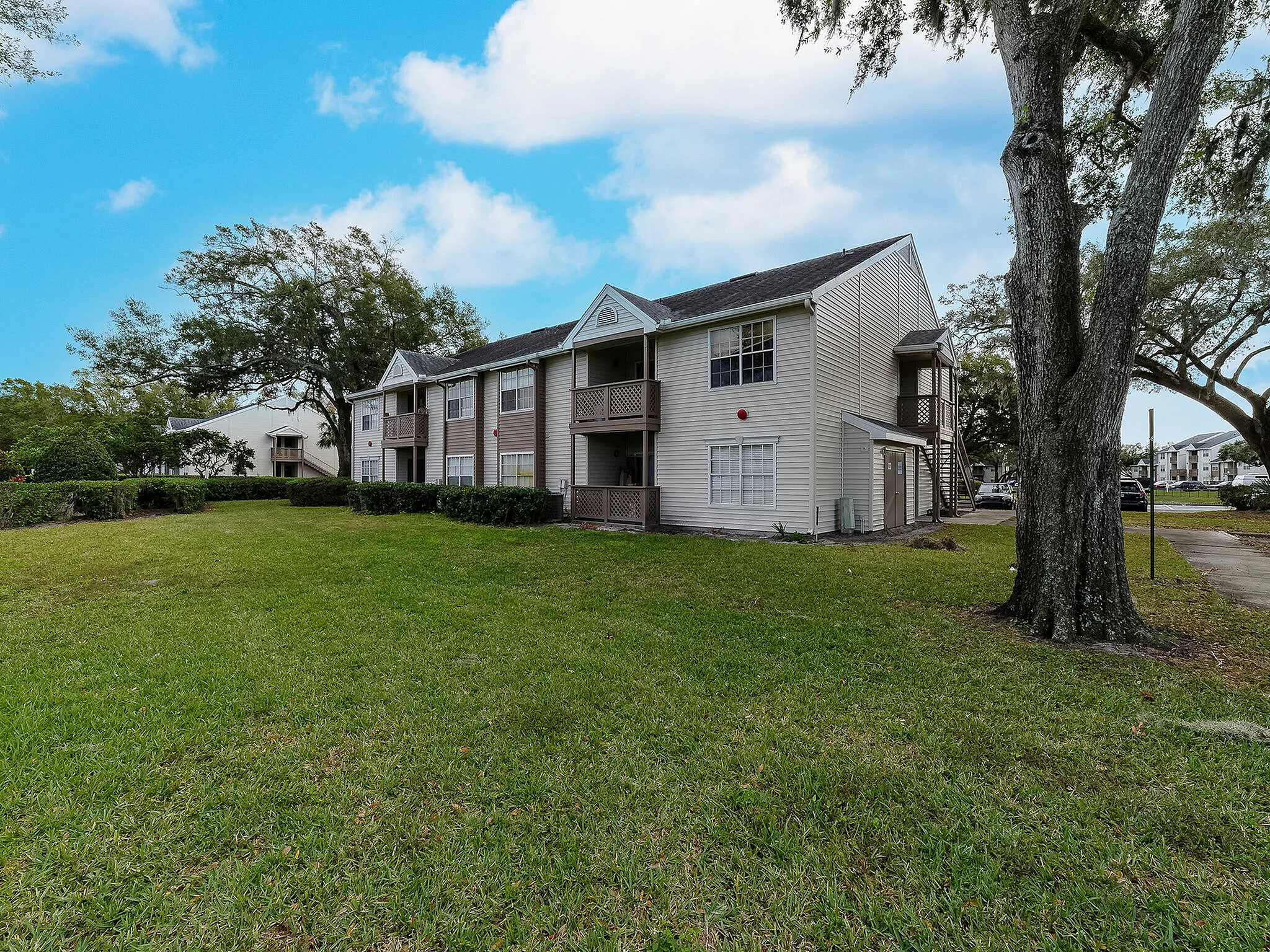Charming two-story apartment complex with lush green lawn and mature trees under a clear blue sky.