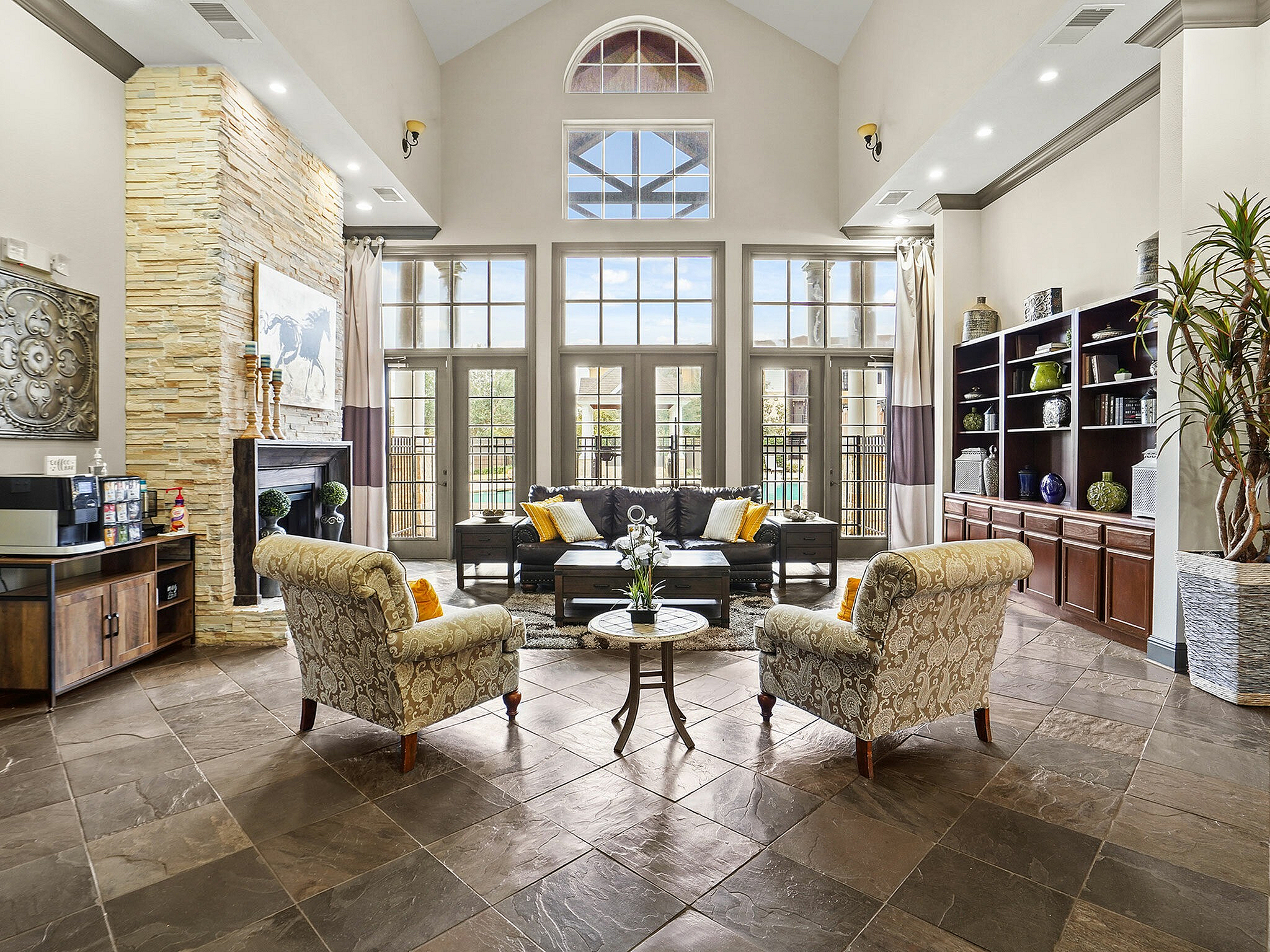 Luxurious living room with high ceilings, natural light, and chic decor featuring a stone fireplace and comfortable seating.