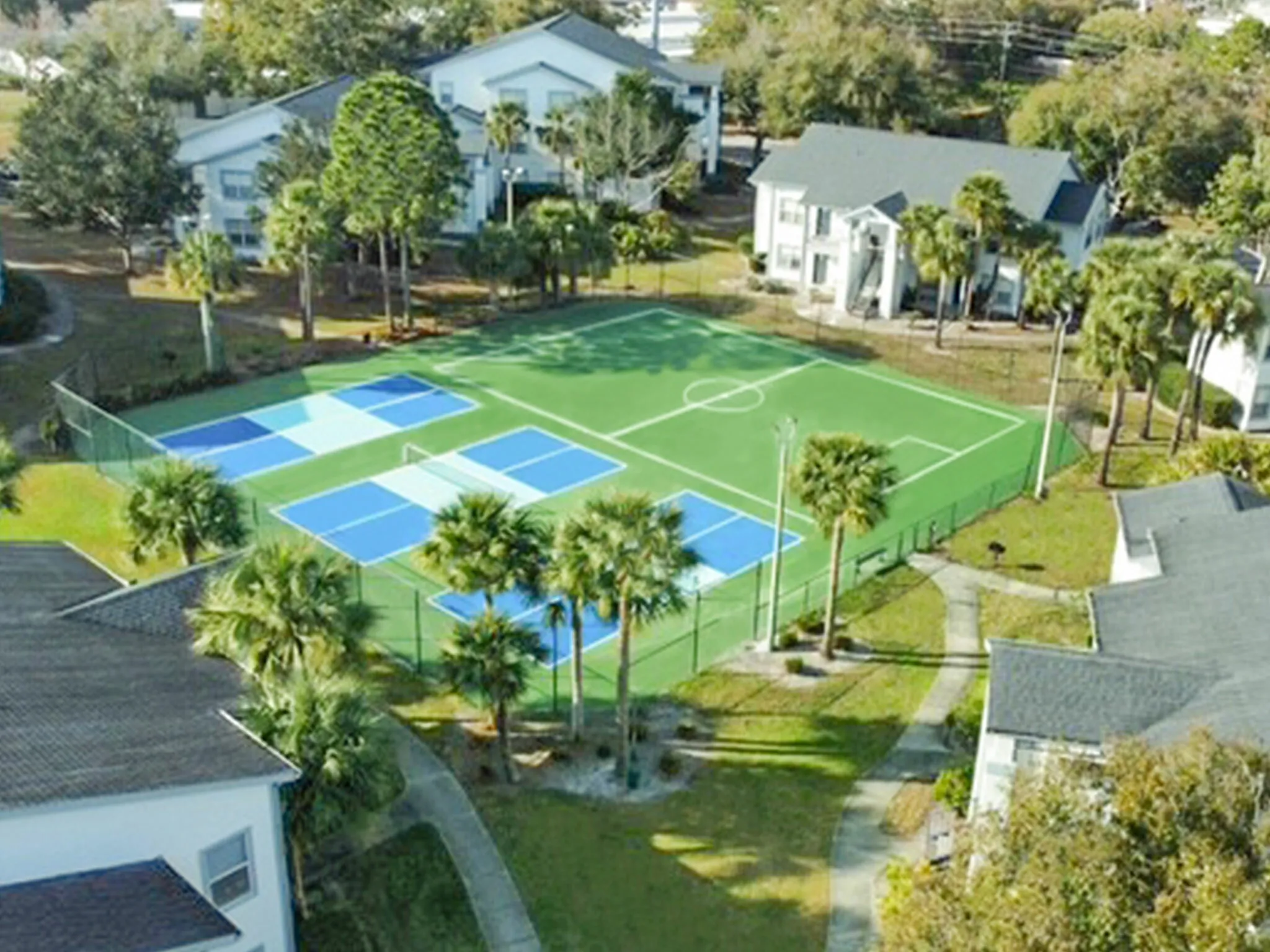 Aerial view of a residential community with lush greenery, tennis courts, and well-maintained pathways.