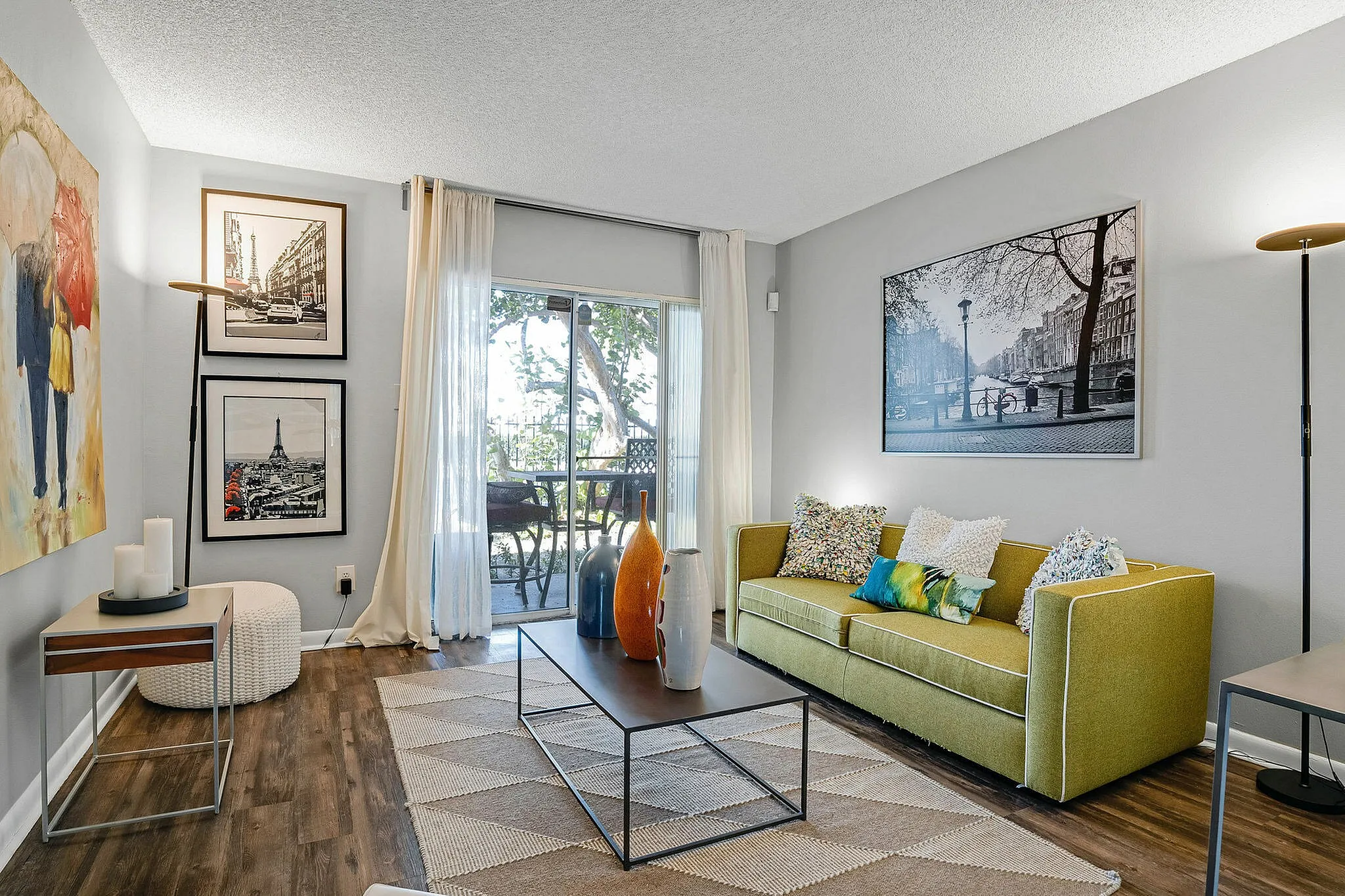 Chic living room with elegant decor, featuring vibrant artwork, stylish green sofa, and natural light from large sliding glass doors opening to a patio.