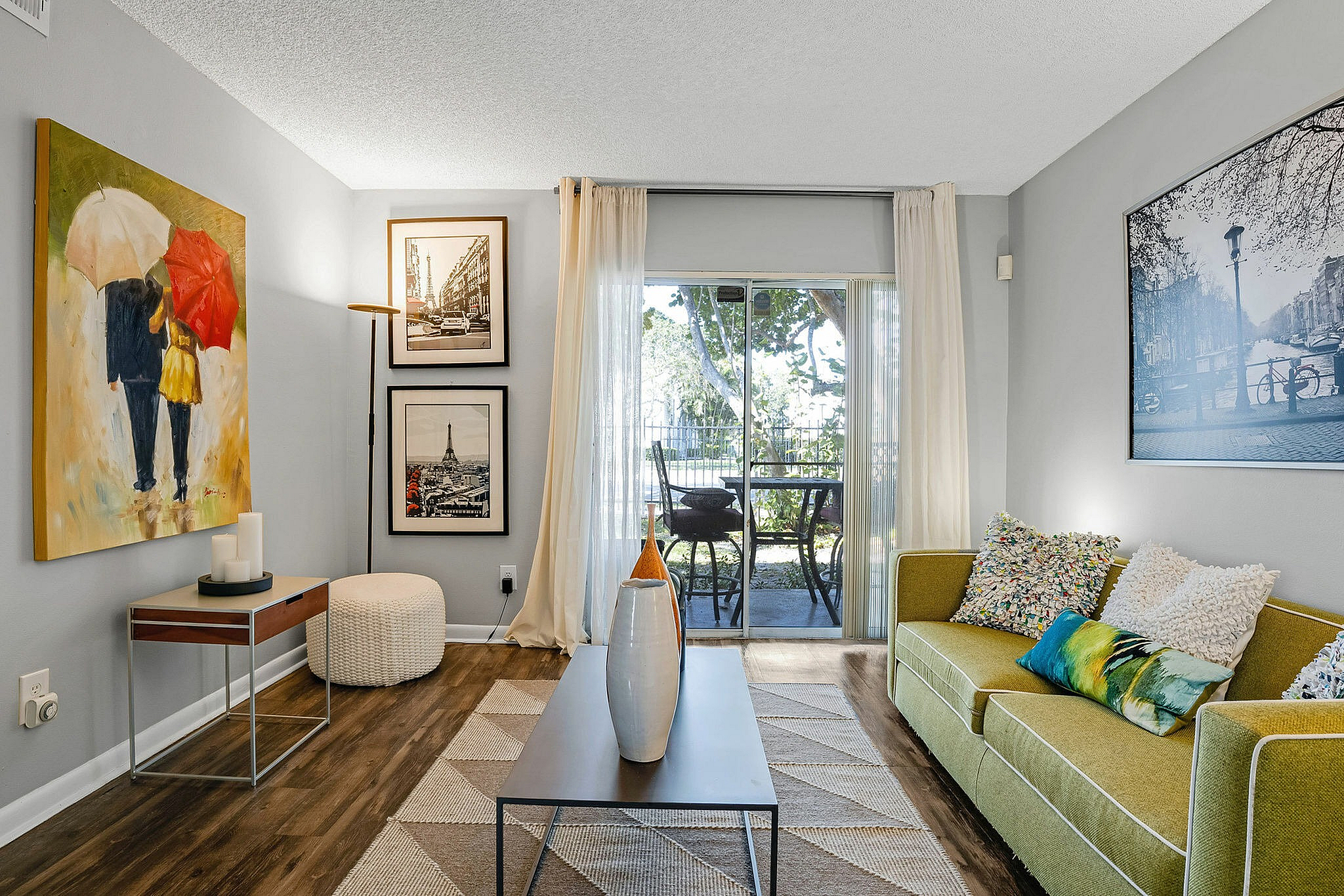 Charming living room with contemporary art, cozy green sofa, and a glass door leading to a scenic balcony.