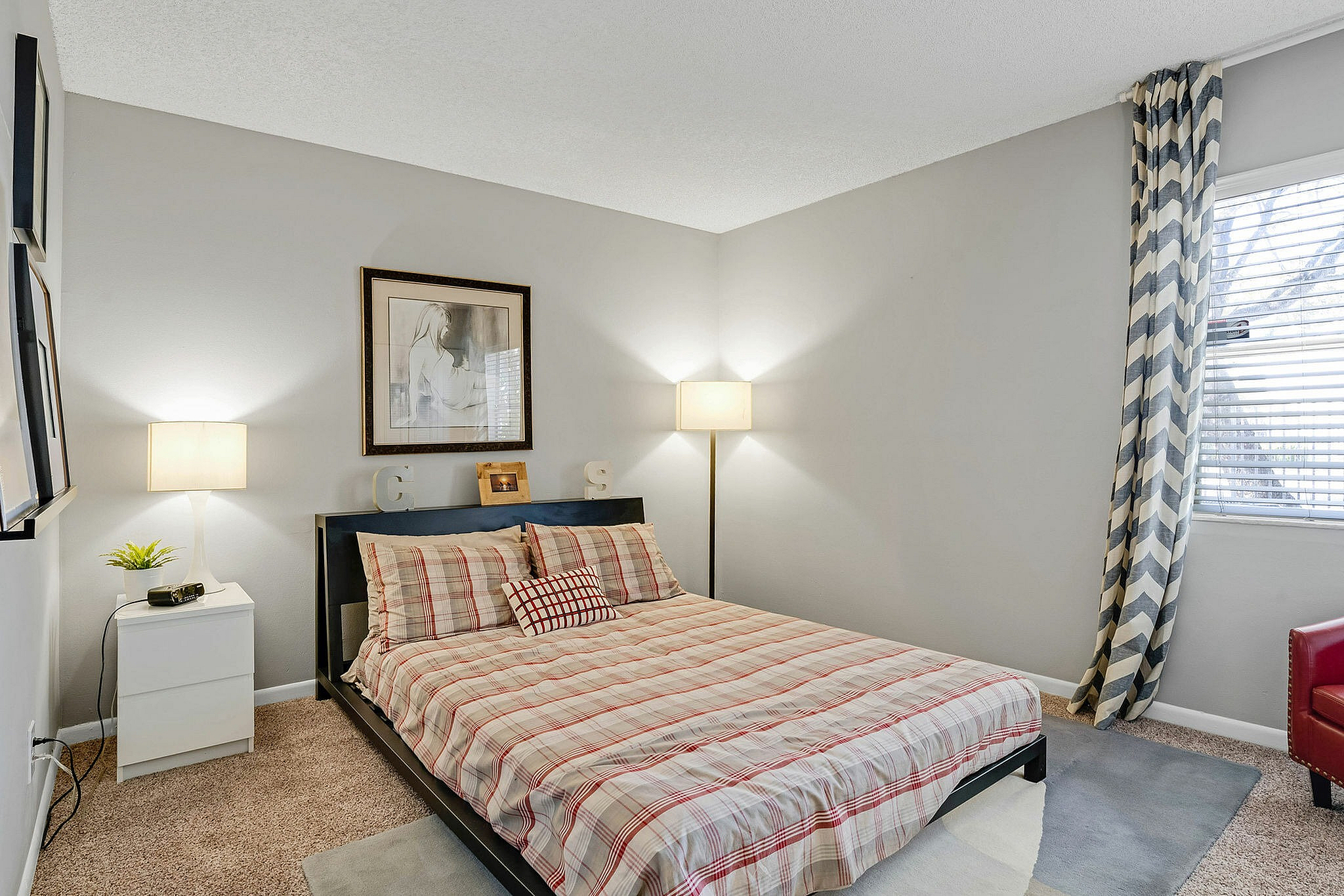 Cozy bedroom with modern decor, featuring a plaid-patterned bed, stylish lamps, and a window with natural light.
