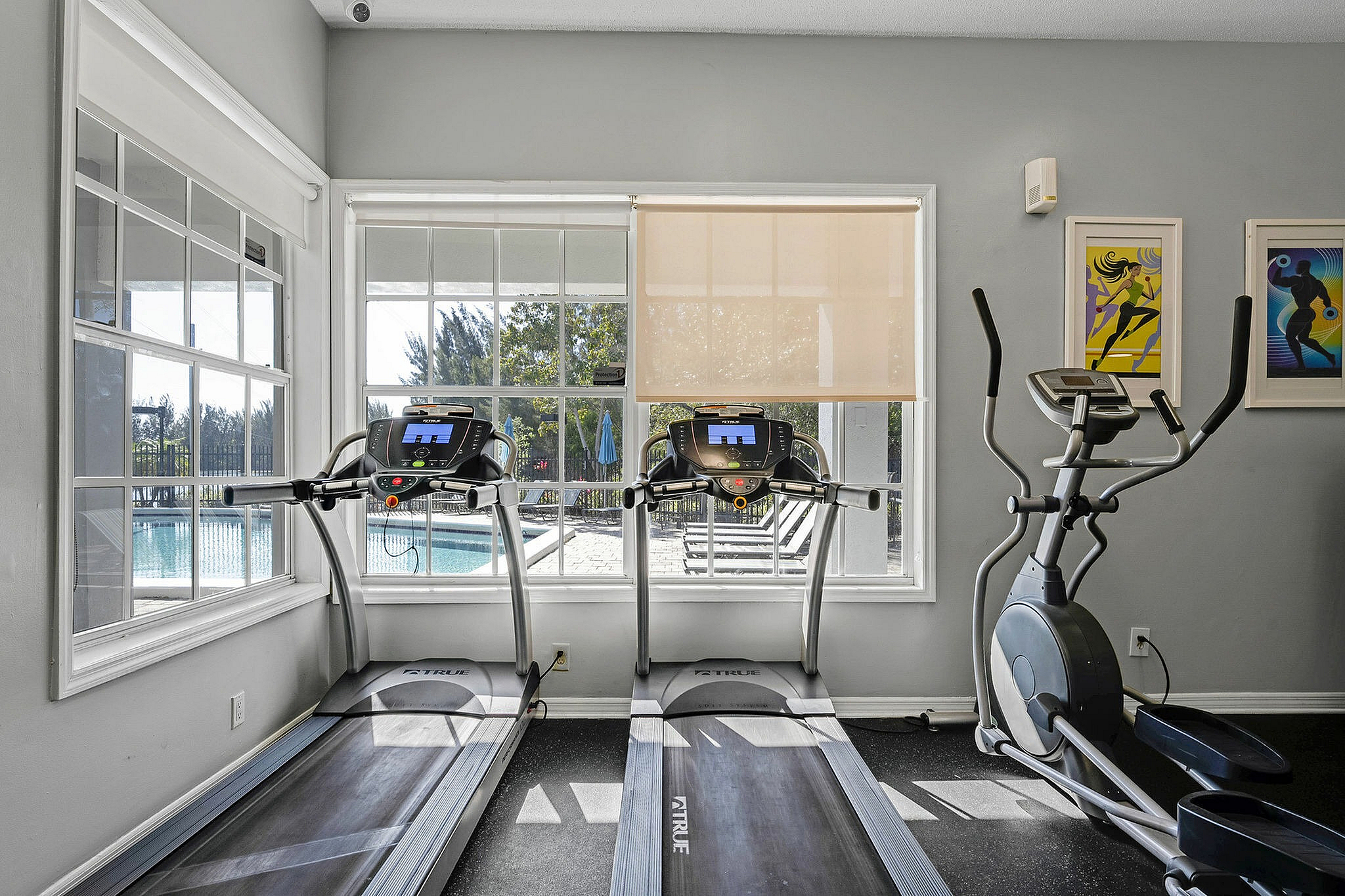 Modern fitness center with treadmills and an elliptical overlooking a sunlit pool area, ideal for energizing workouts.