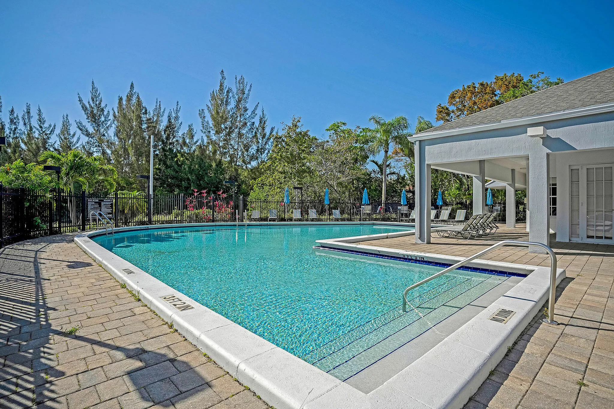 Inviting outdoor pool area with clear blue water, surrounded by lush greenery and sun loungers under a bright sky.